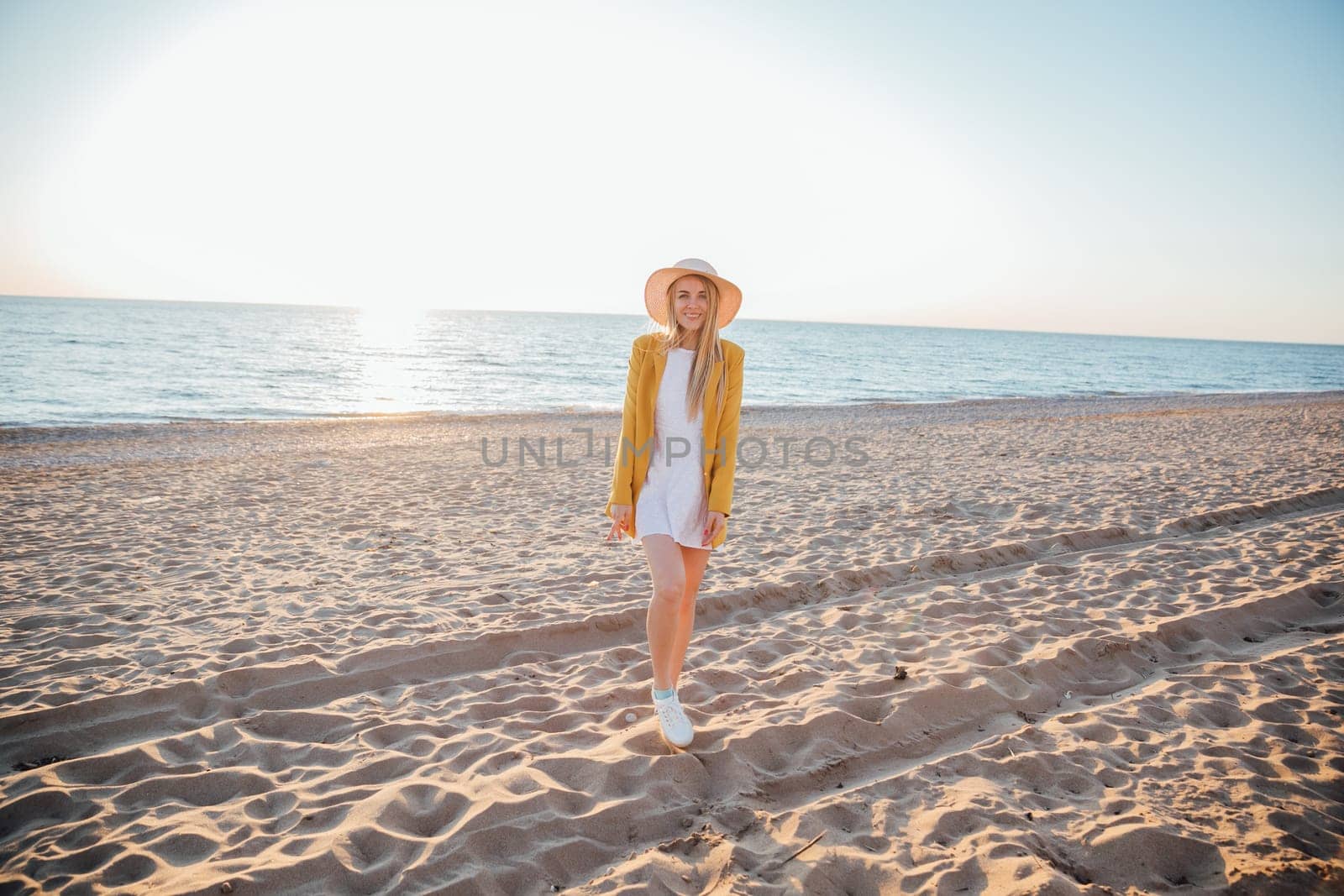 Beautiful blonde woman in summer dress walking on the beach by the sea