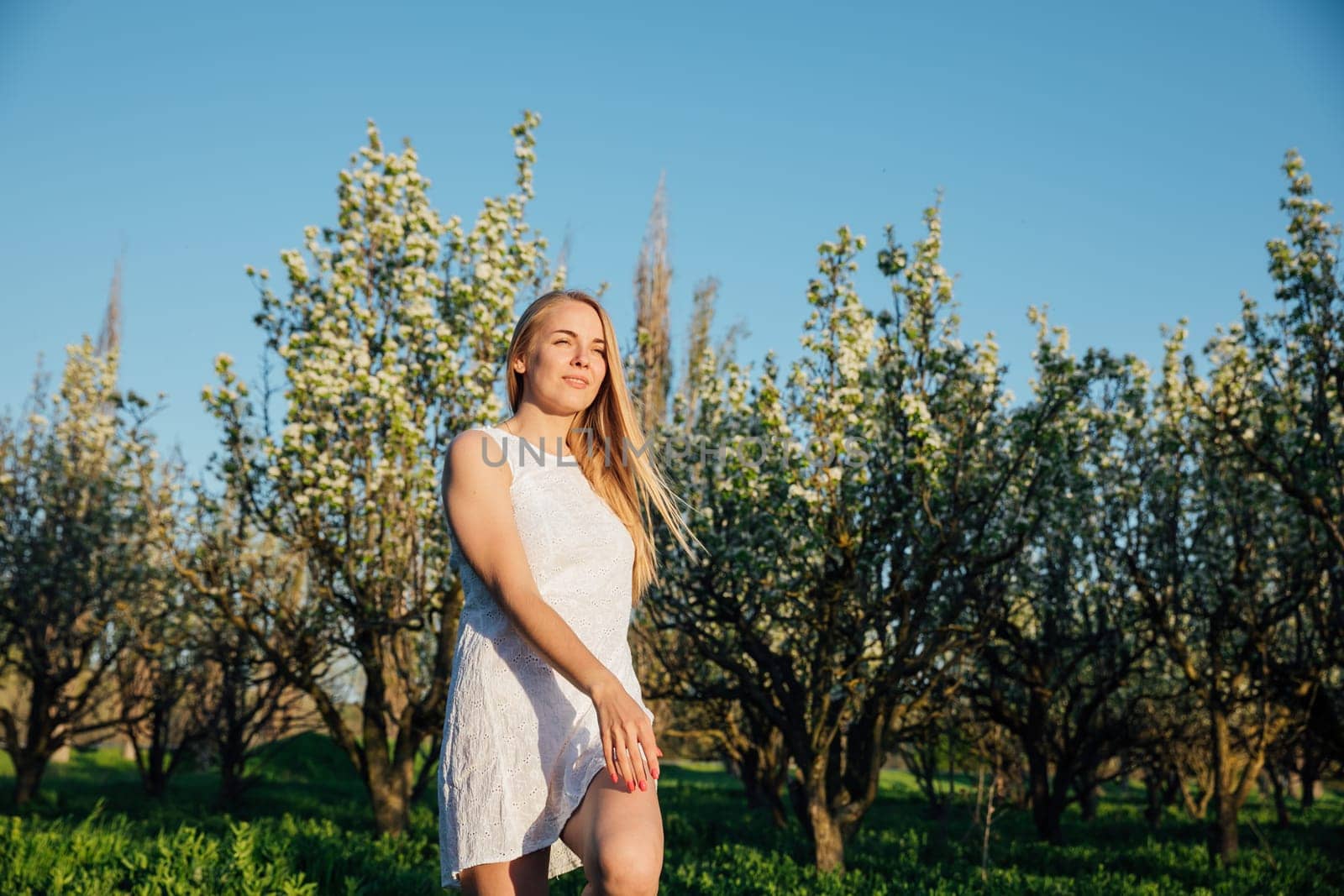 Blonde woman in summer dress walking in blooming garden in spring