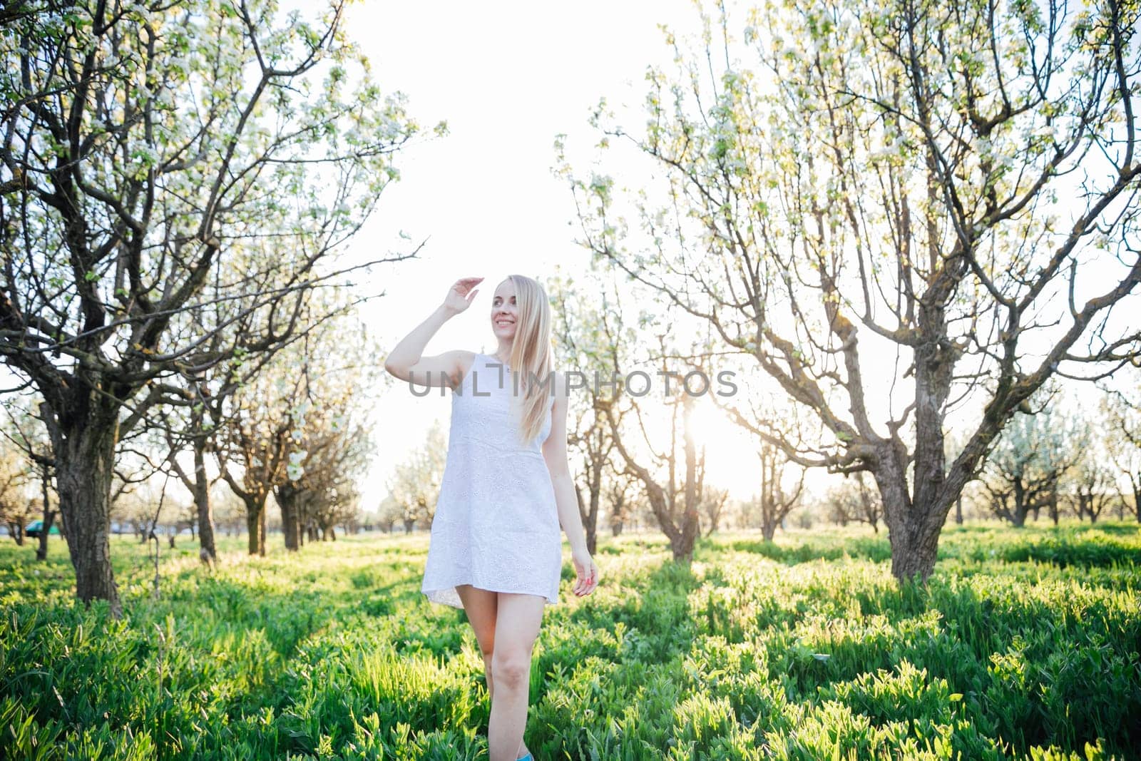 Blonde woman in summer dress walking in blooming garden in spring