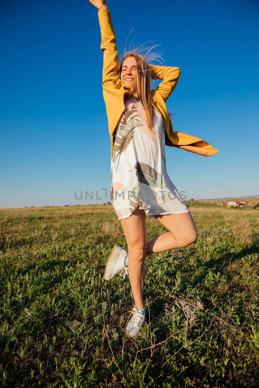 Woman in summer dress laughing and running on green field at sunset
