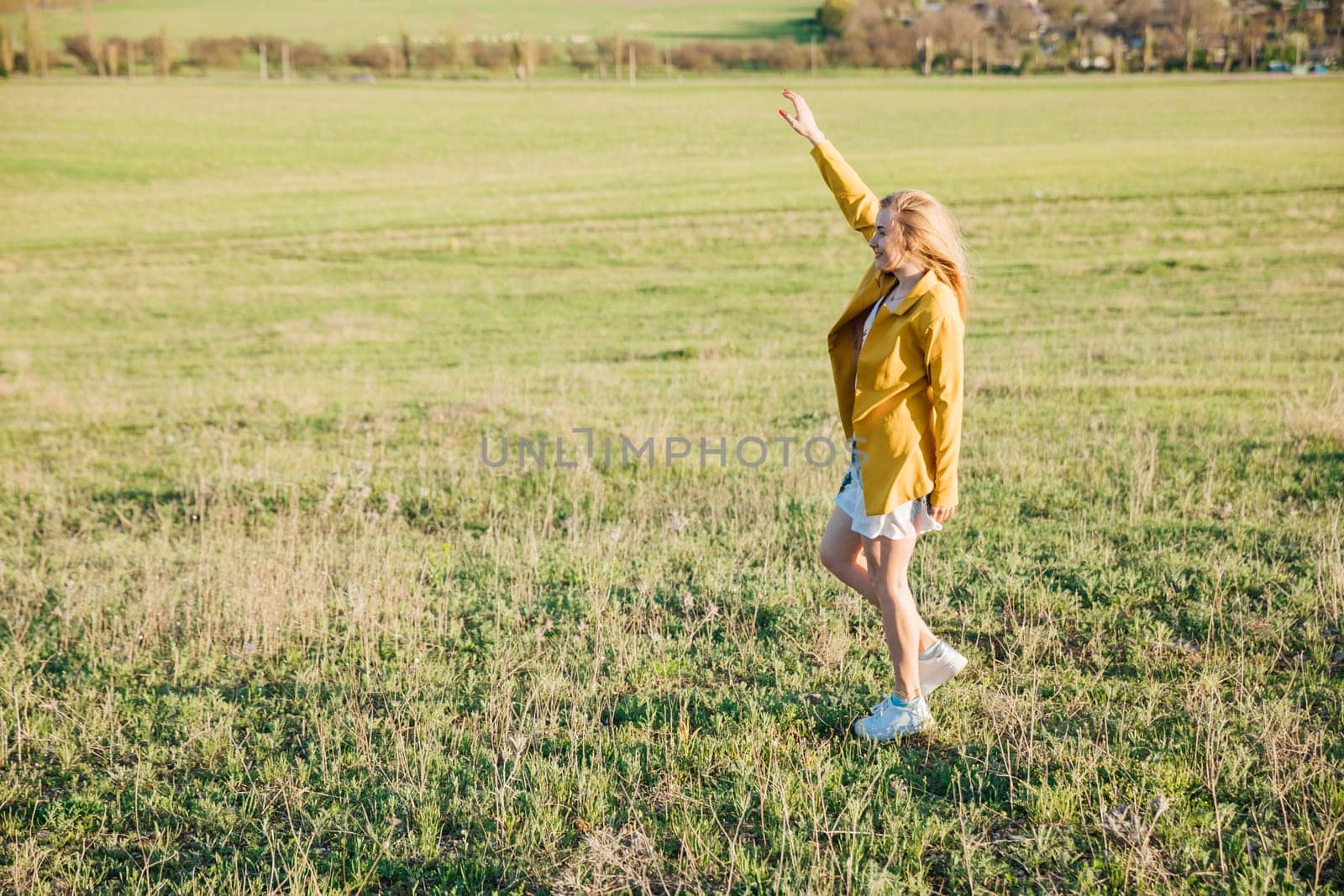 Woman in summer dress laughing and running on green field at sunset