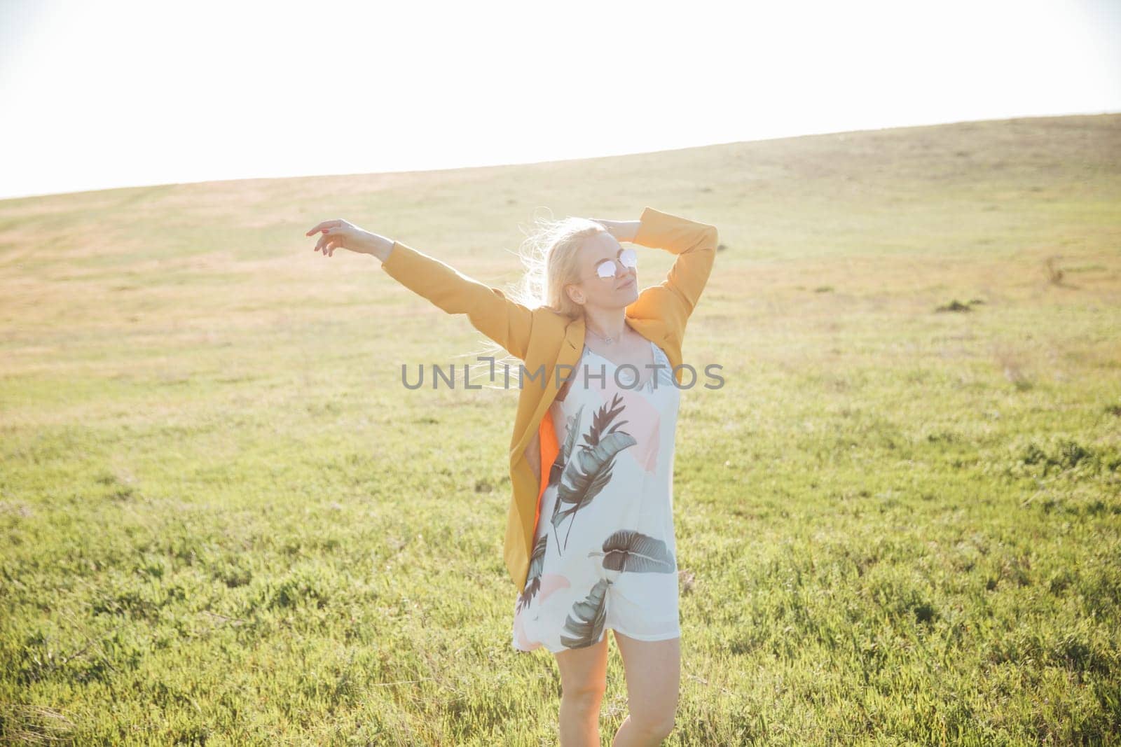 Woman in summer dress laughing at sunset on green field
