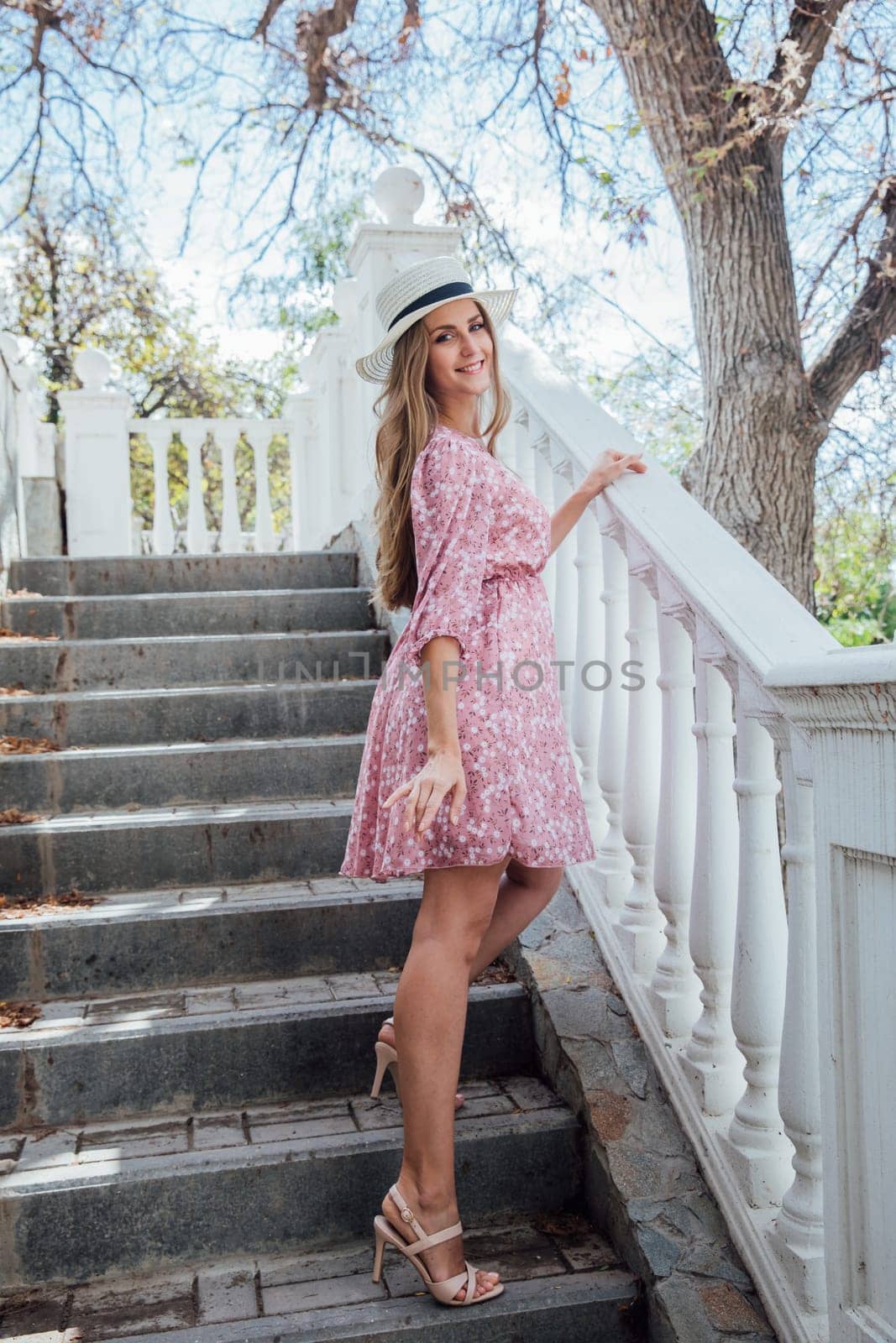 Blonde woman in summer pink dress and hat on street smiling