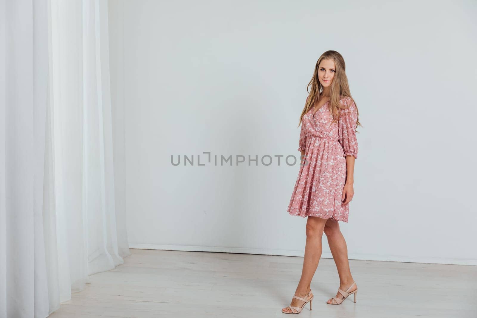 Beautiful fashionable blonde woman in summer pink dress on white background