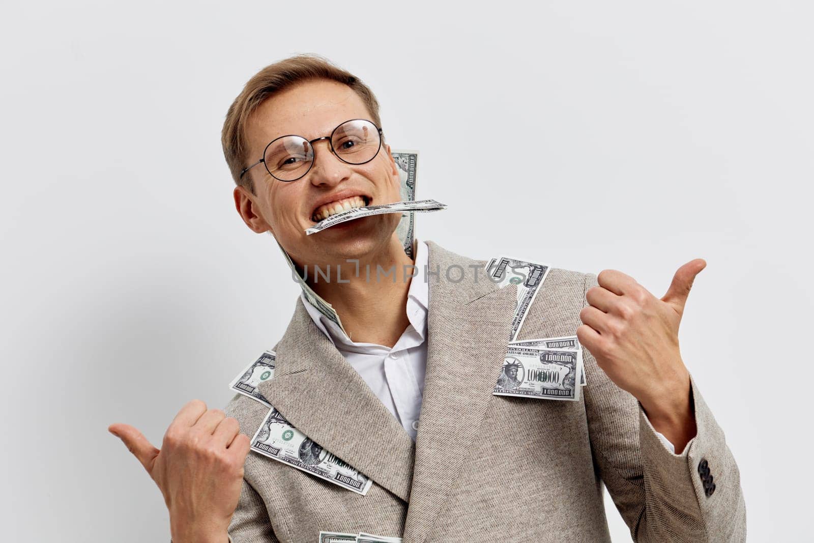 Cheerful man wearing glasses and a beige suit decorated with dollar bills, smiling widely while holding a toothbrush in his mouth and giving thumbs up, against a clean white backdrop. Concept: humor, money, business casual, playful attitude, financial success.