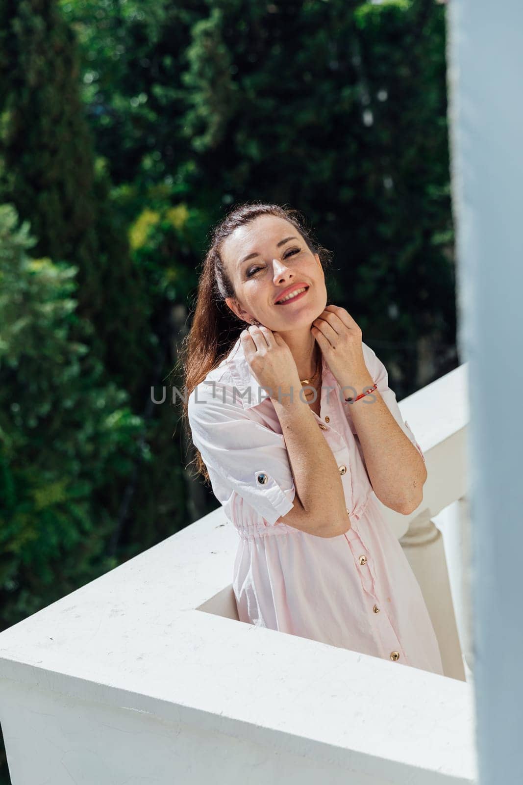 Brunette woman in summer pink dress on the balcony of the house smiling