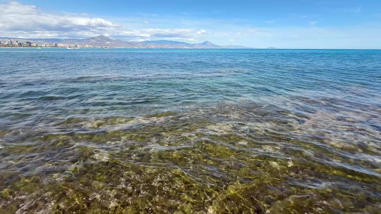 A serene and tranquil coastal scene showcasing crystal clear blue waters, rocky shores, and distant majestic mountains