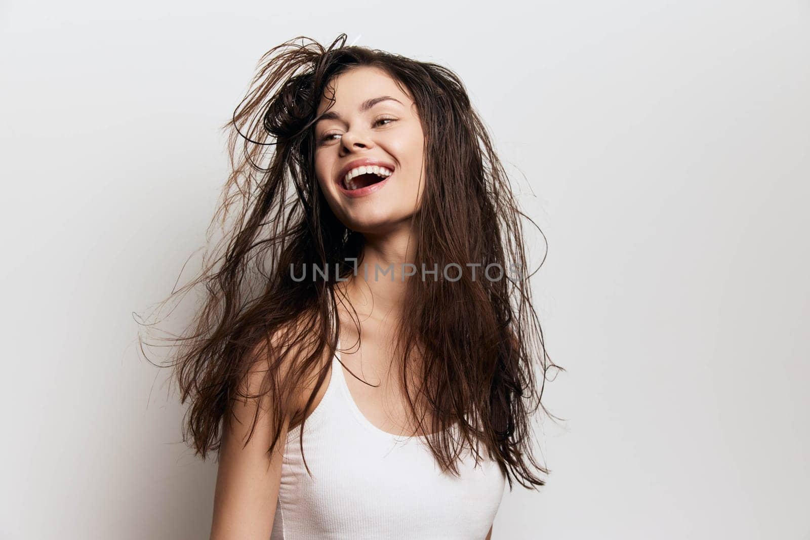 cheerful young girl with flowing hair laughing joyfully, featuring a fresh and lively expression on a neutral light backdrop, symbolizing beauty, freedom, and positivity