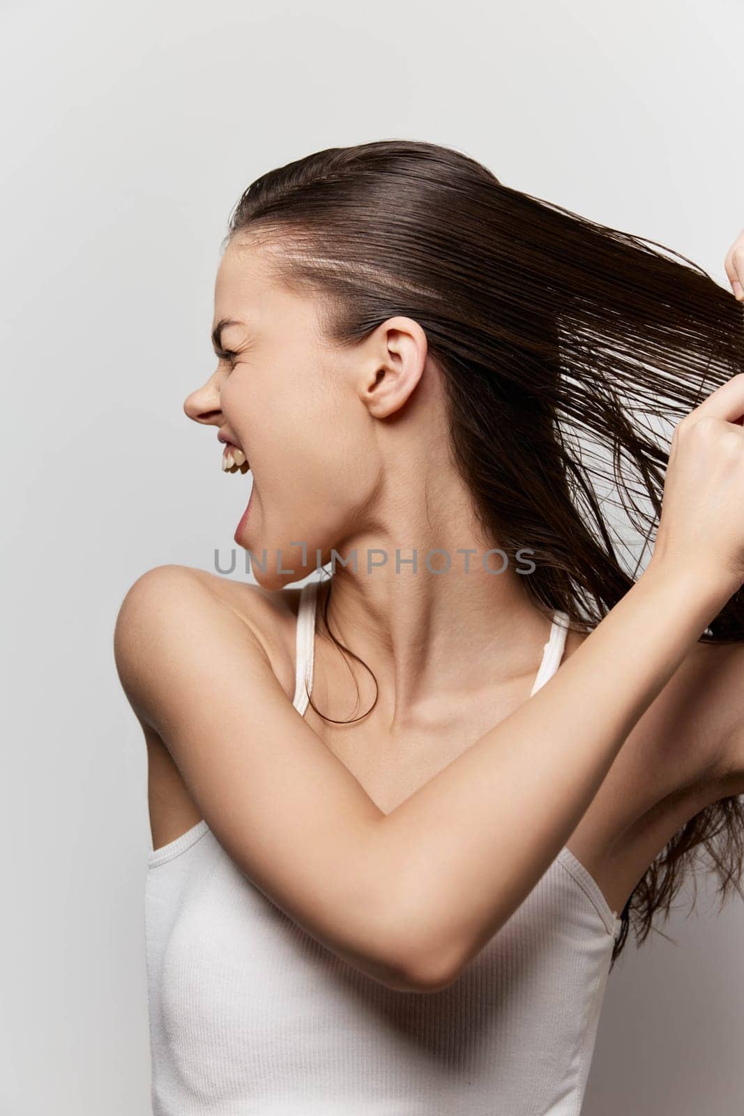 portrait of a smiling young woman joyfully playing with her long hair, against a soft gray background, reflecting emotion, energy, and the freedom of self expression in her playful demeanor