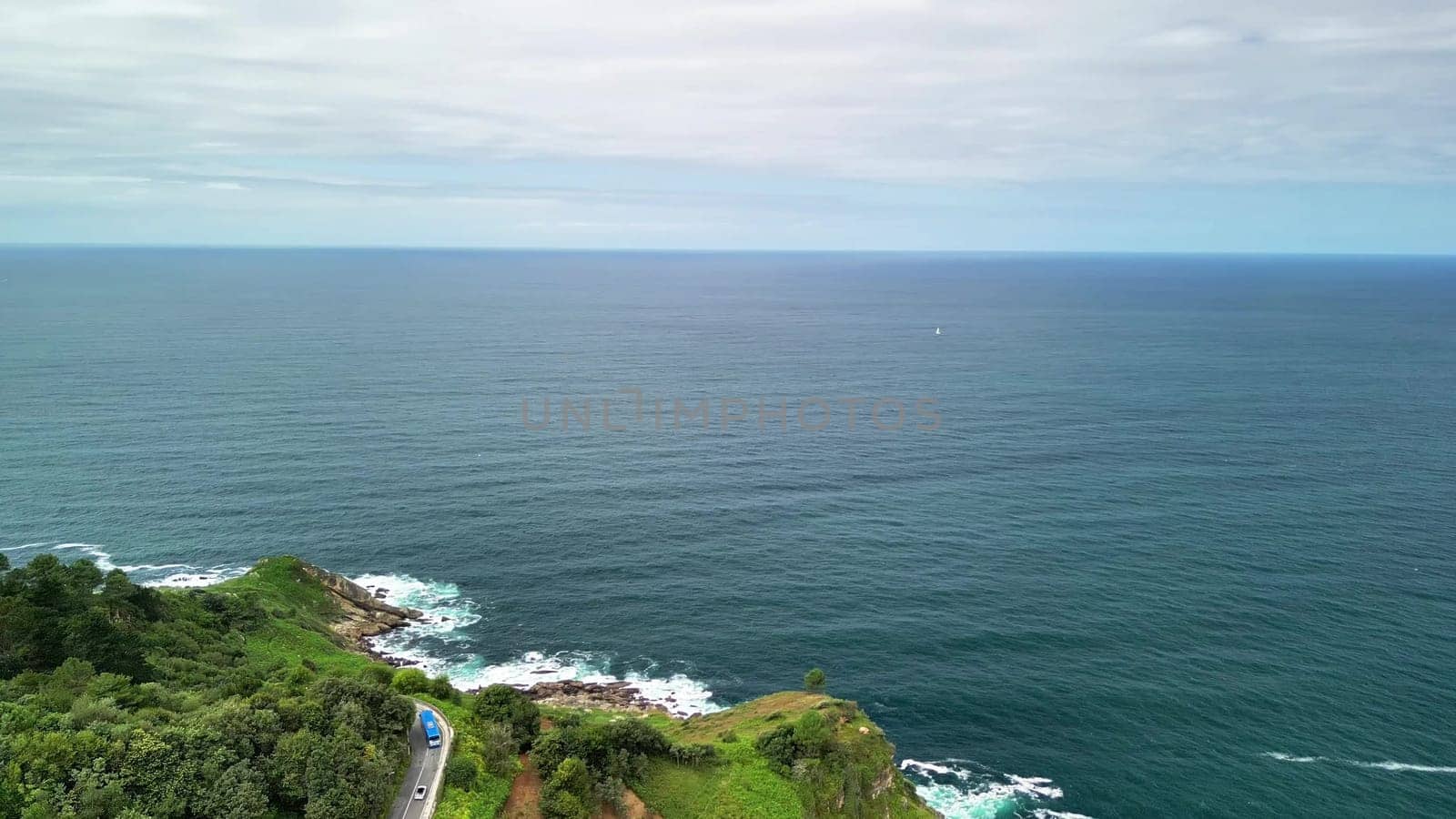 This stunning landscape beautifully features the vast ocean, lush rolling hills, and a peaceful coastal road