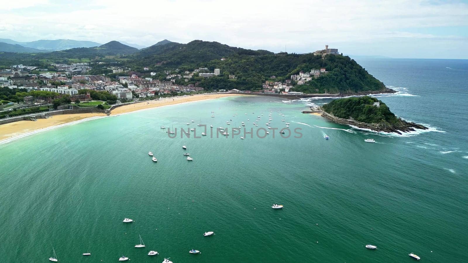 Aerial view of a picturesque beach, surrounded by lush hills, with boats bobbing in sparkling water