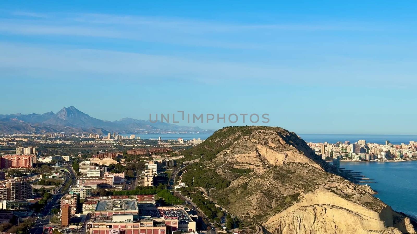 Breathtaking aerial shot of Alicante's coastline and hills, showcasing serene blue waters and vibrant city life.