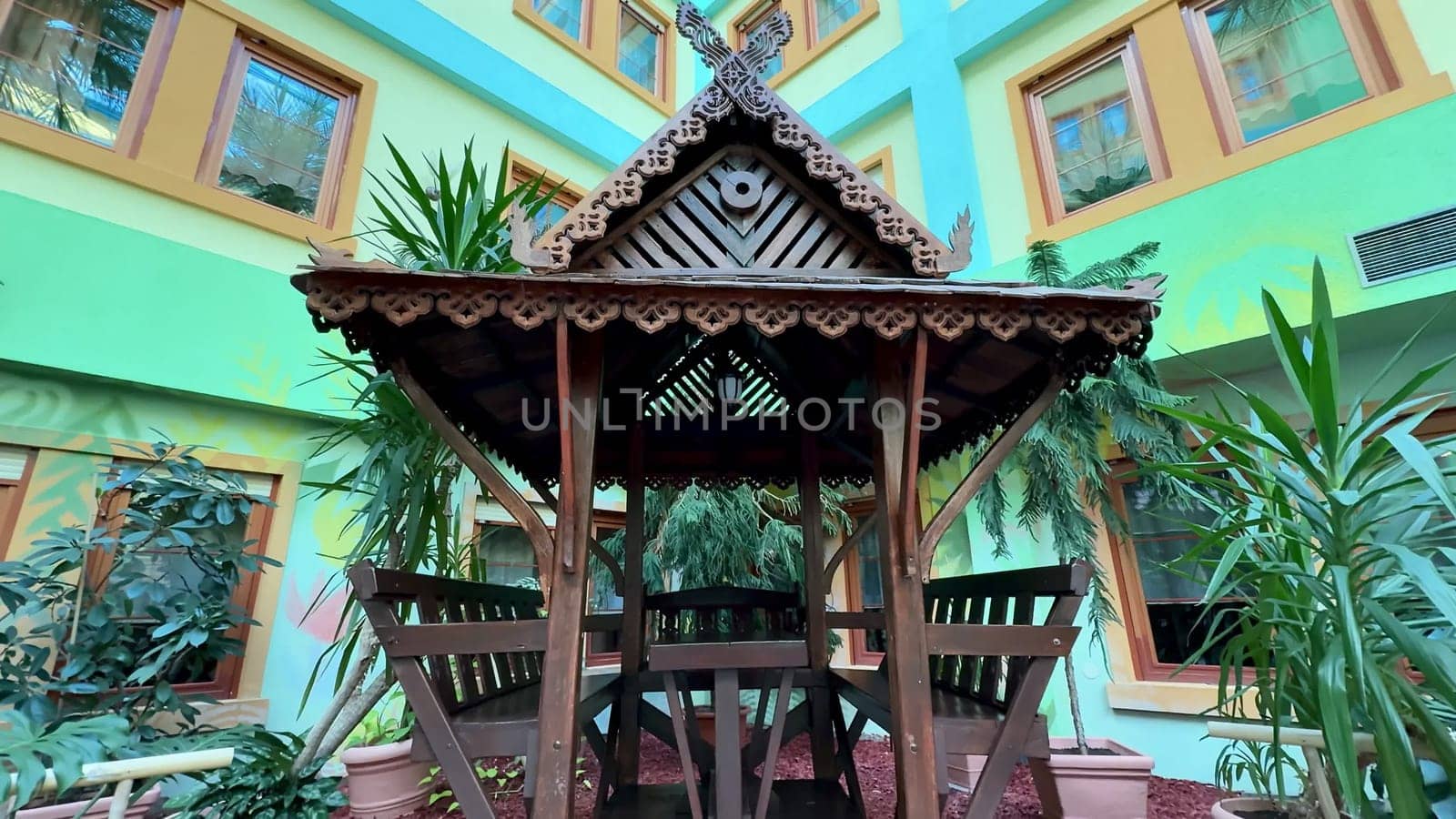 A beautifully designed and crafted wooden gazebo is perfectly nestled among the vibrant greenery in a colorful setting