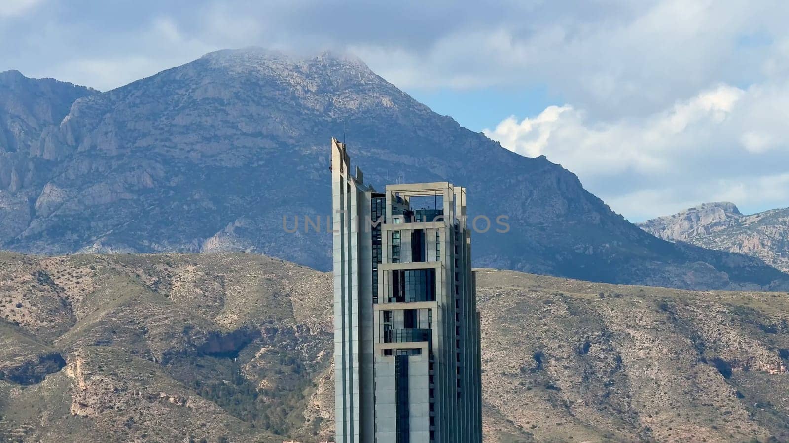 A strikingly impressive skyscraper rises majestically above a picturesque and serene mountainous backdrop
