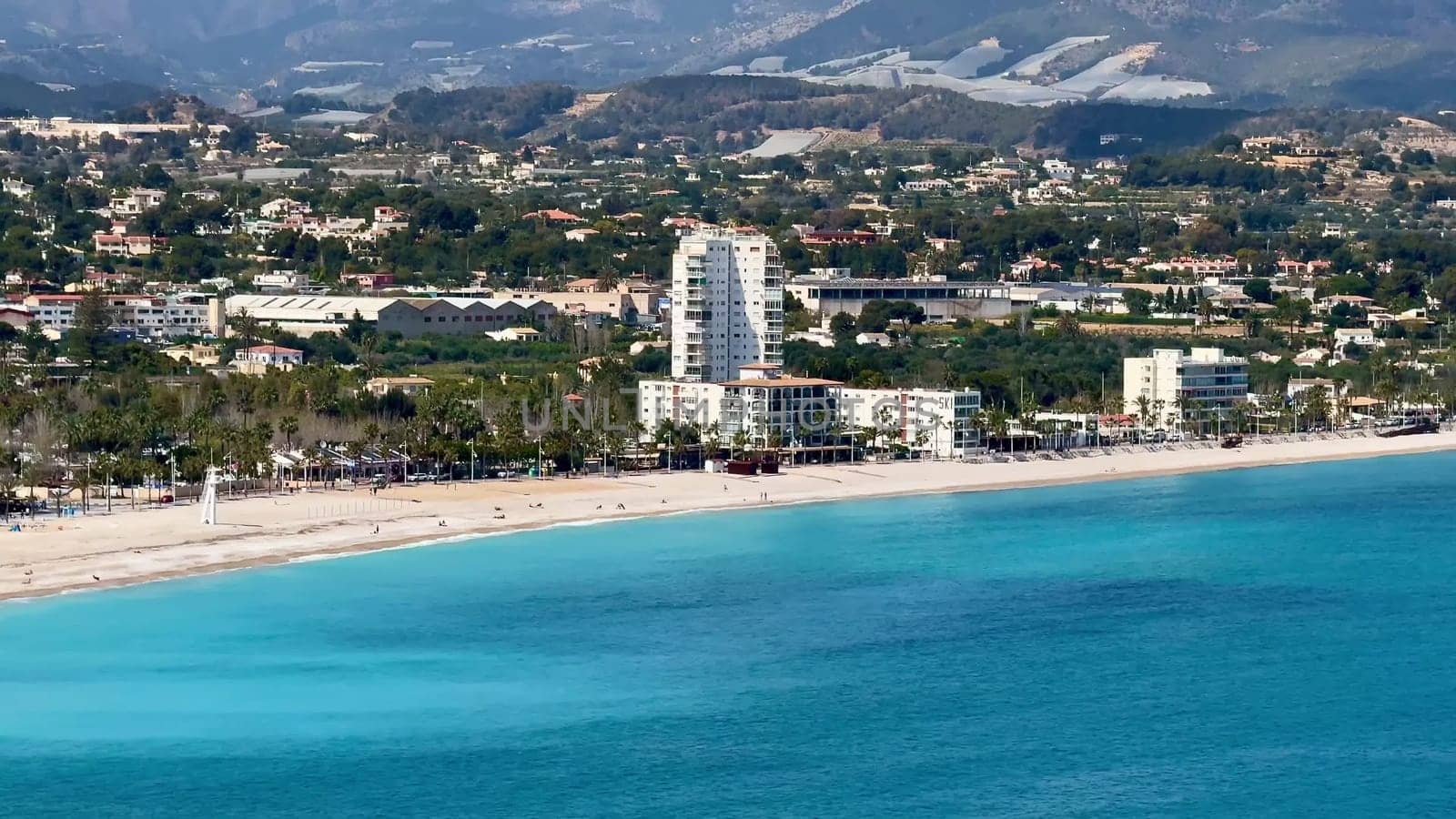 An aerial view shows a serene beach with clear turquoise waters and beautiful beachfront properties