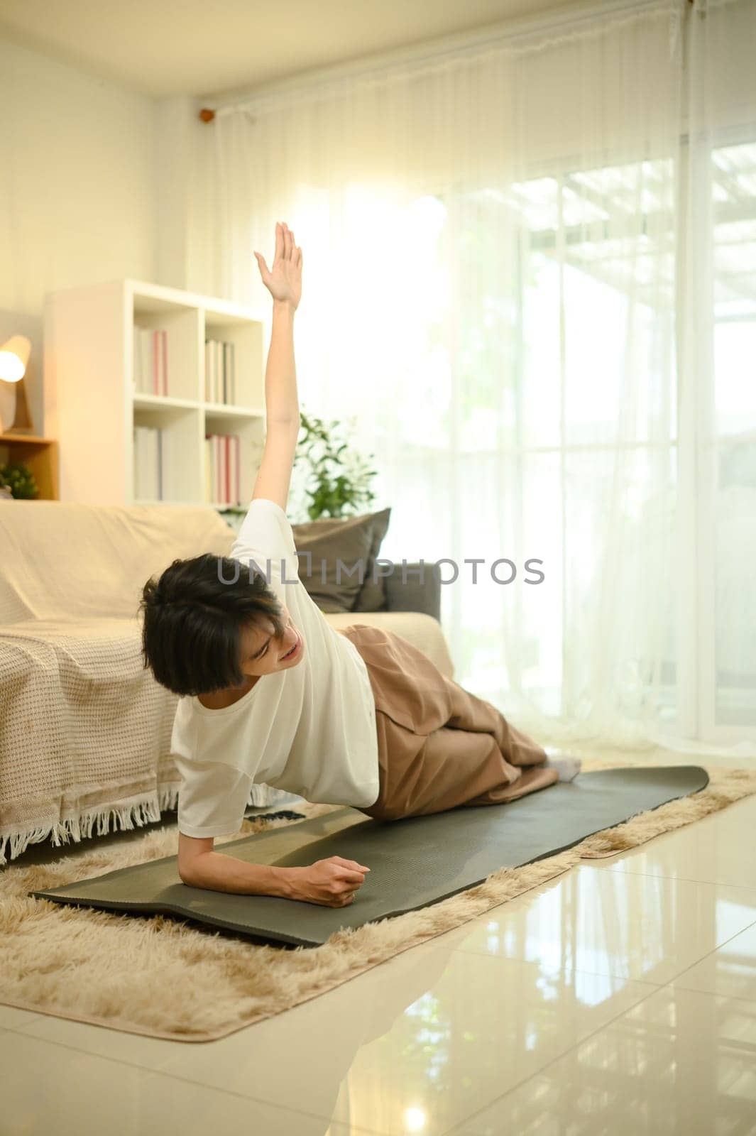 Young man doing a side plank exercise on a yoga mat in a living room.