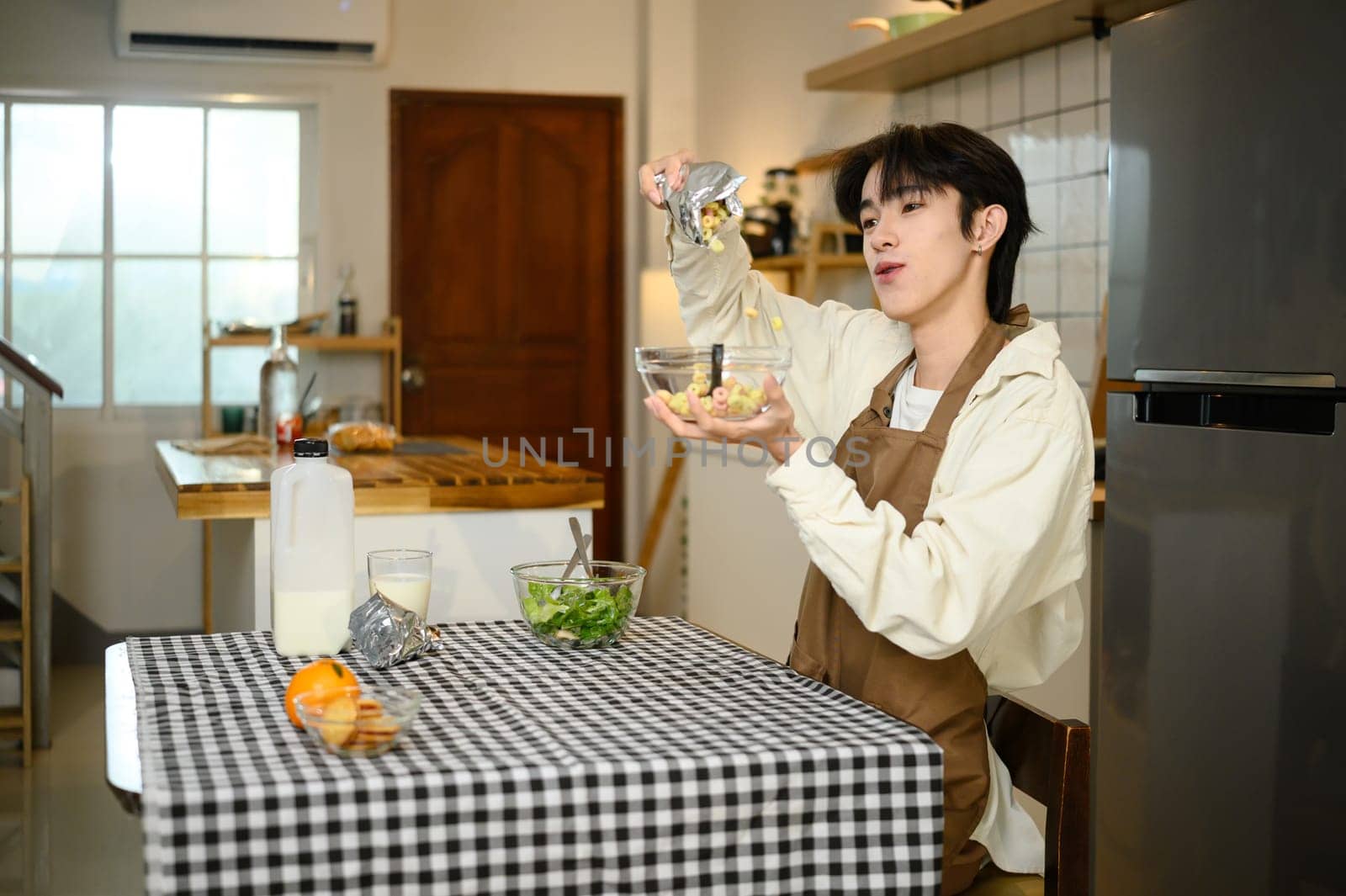 Smiling man enjoying breakfast with cereal and milk in a bright kitchen.