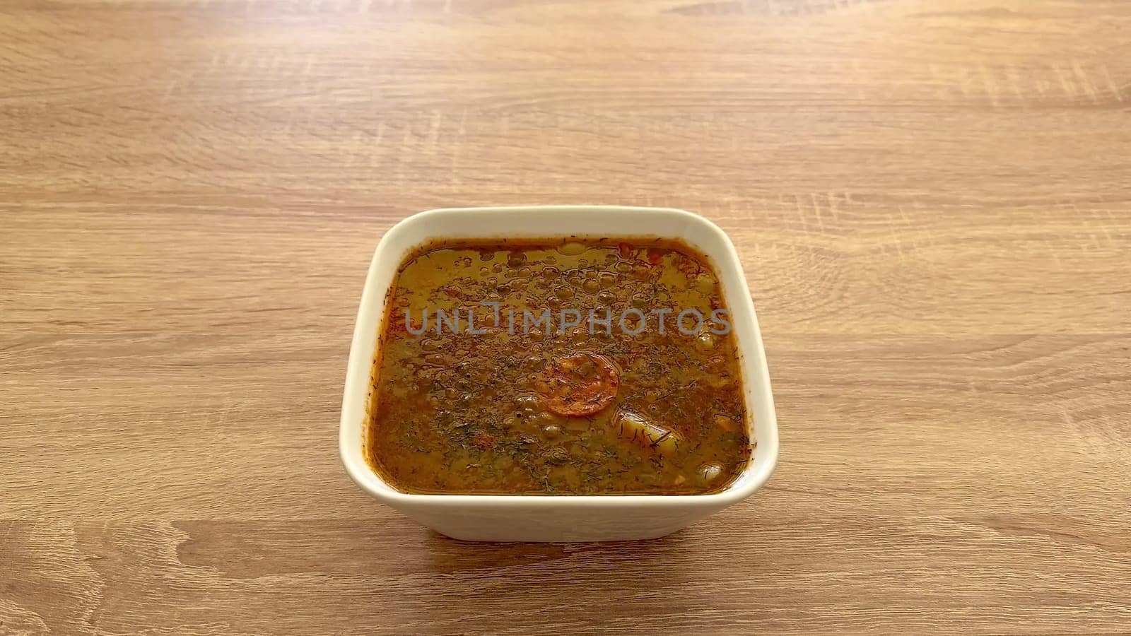 A vibrant and colorful herbal soup served in a pristine white bowl, finely presented on a rustic wooden surface