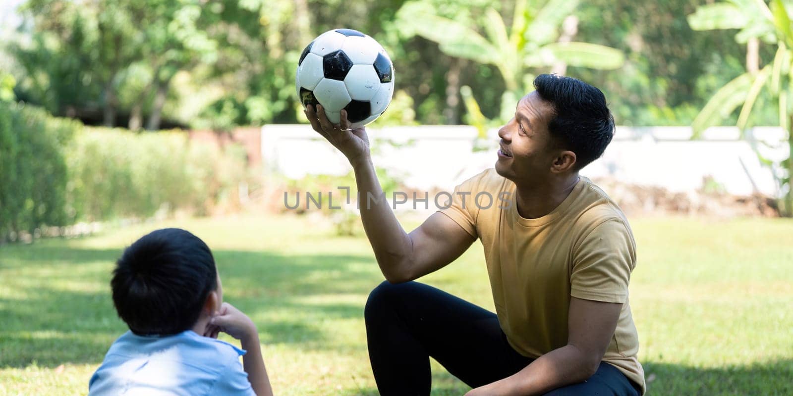 A father playfully teaching his son soccer skills, encouraging wellness and teamwork in their outdoor garden setting, filled with joy and laughter.
