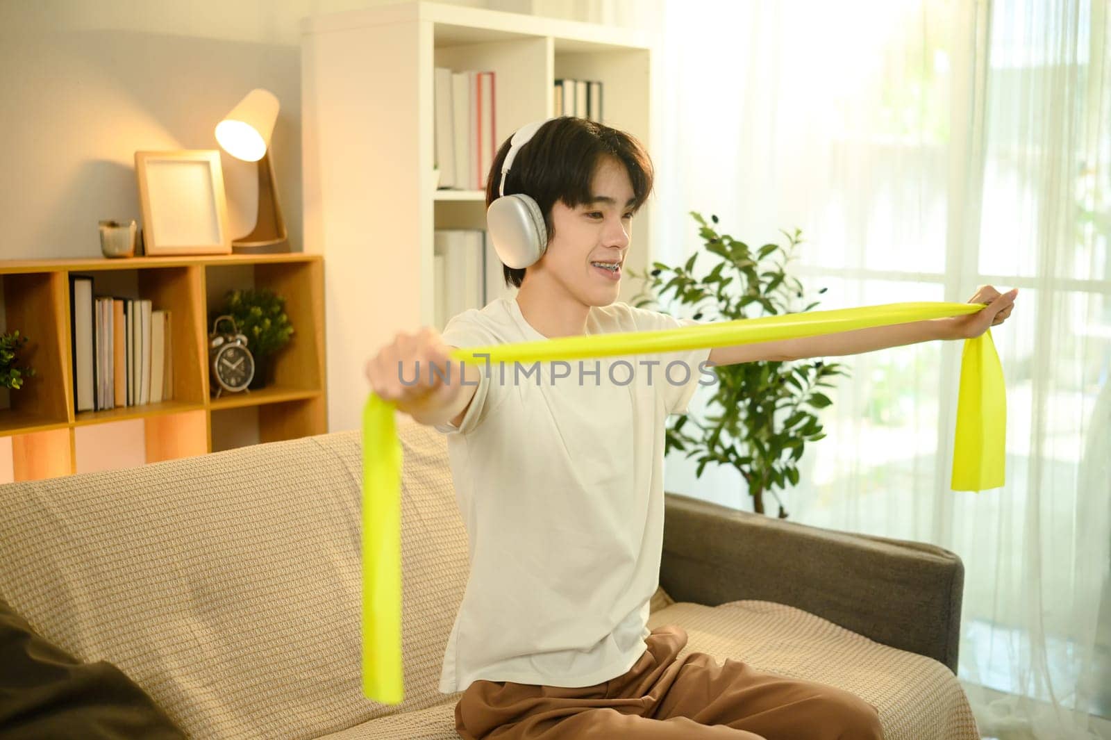 Smiling man in headphones working out with resistance band in a living room.
