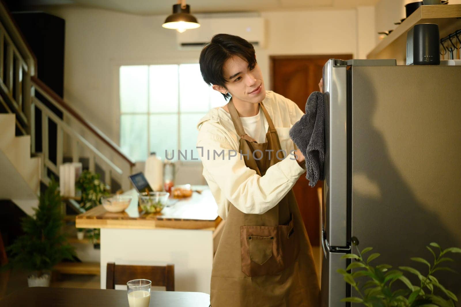 Smiling man doing household chores, cleaning the refrigerator with a cloth.