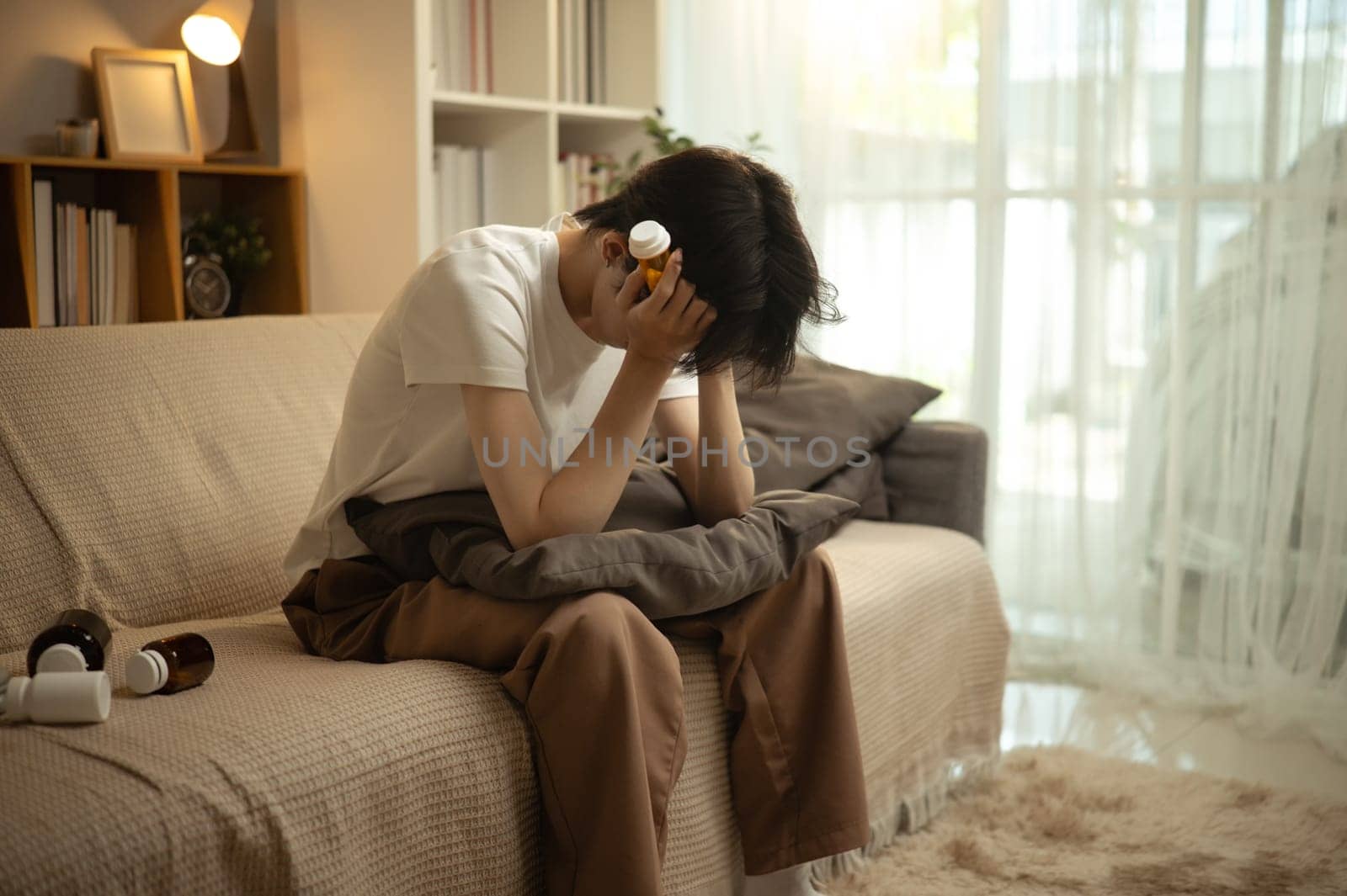 Sad man in a dimly lit living room appearing overwhelmed and anxious with pills in hand.