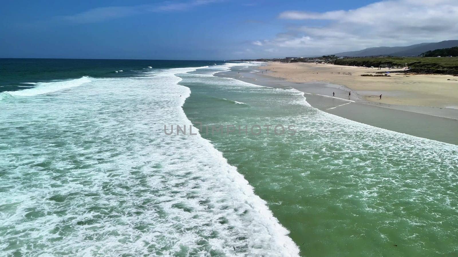 Stunning aerial view showcasing the mesmerizing waves crashing upon a sandy beach beneath a pristine, clear blue sky