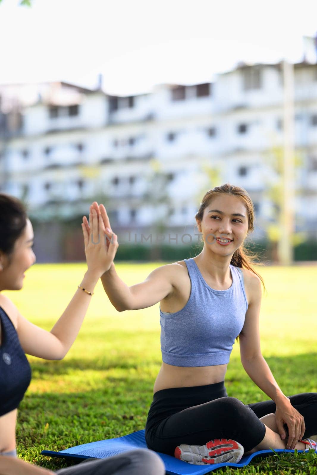 Two happy women giving a high five after successful outdoor workout session on mats.