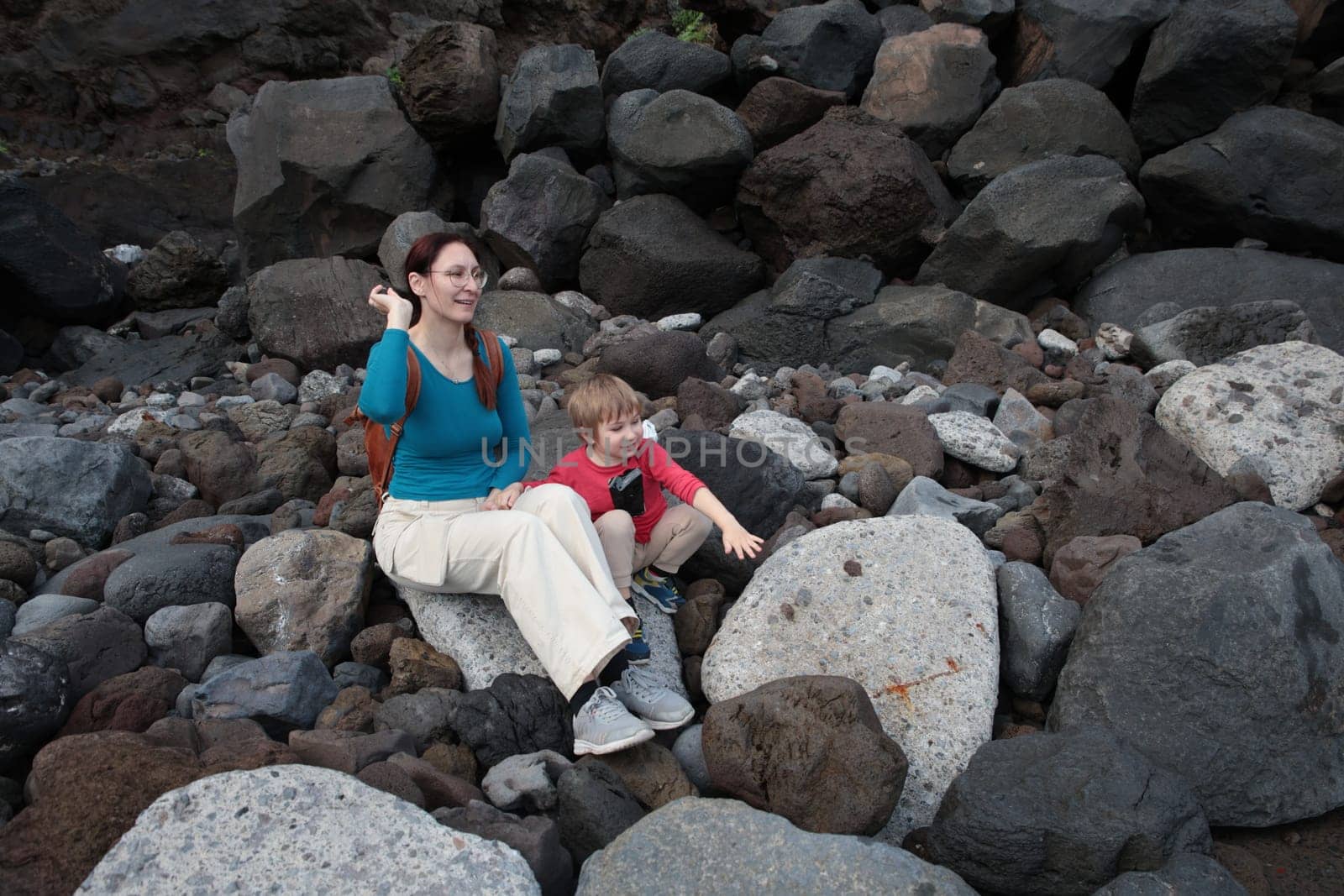 Mother and son sitting on rocks, enjoying the scenery on a rocky beach