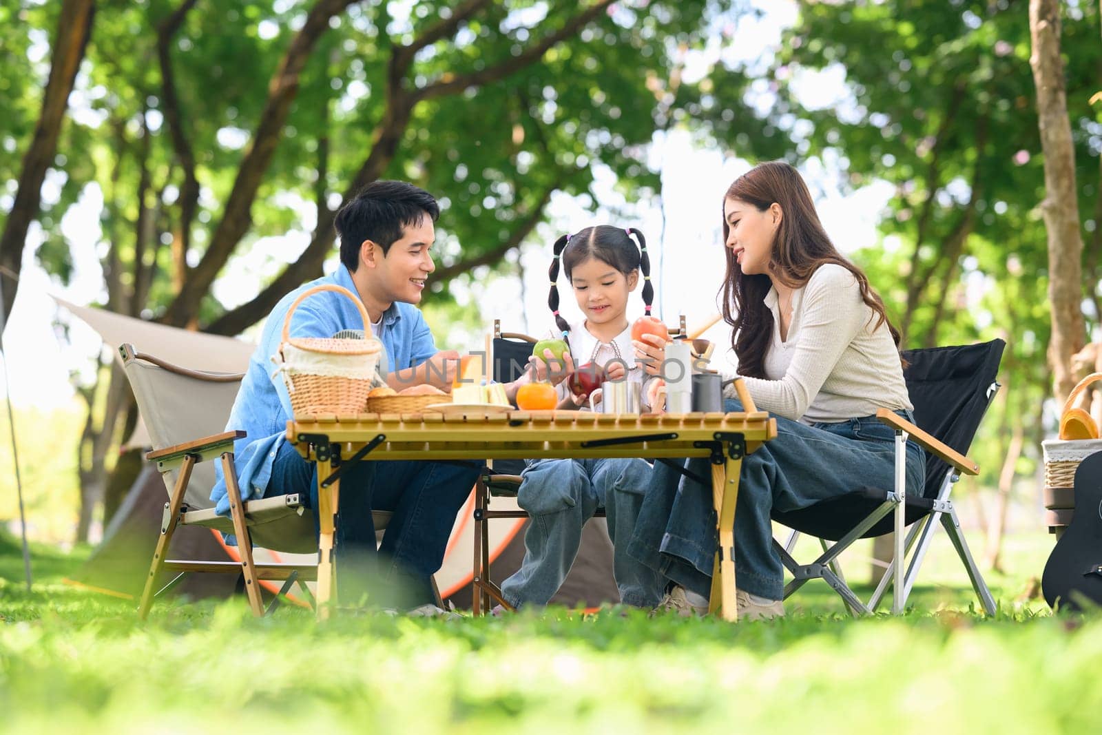 Happy family enjoying breakfast at a table while camping in a forest park.