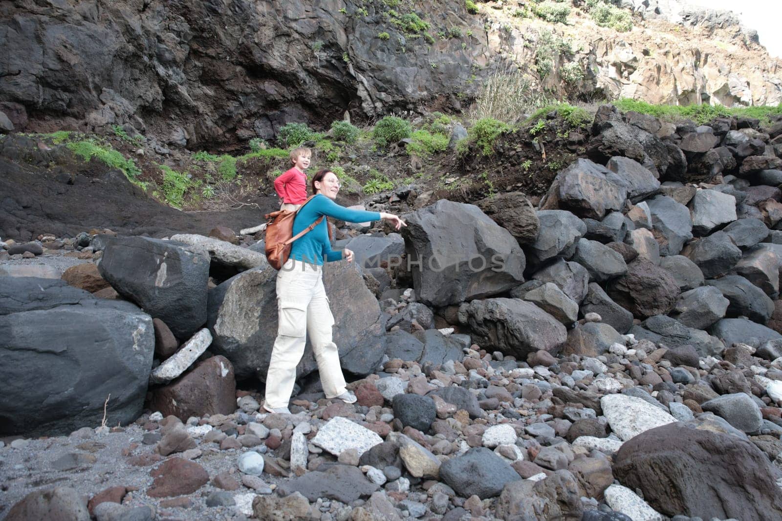 Woman pointing to something while hiking with her child on a rocky beach
