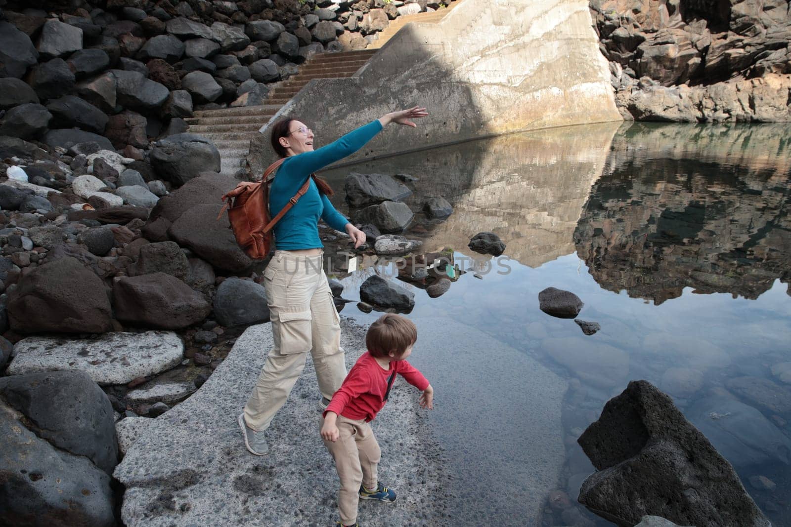 Tourist and child enjoying natural pool in rocky volcanic landscape, exploring nature during vacation