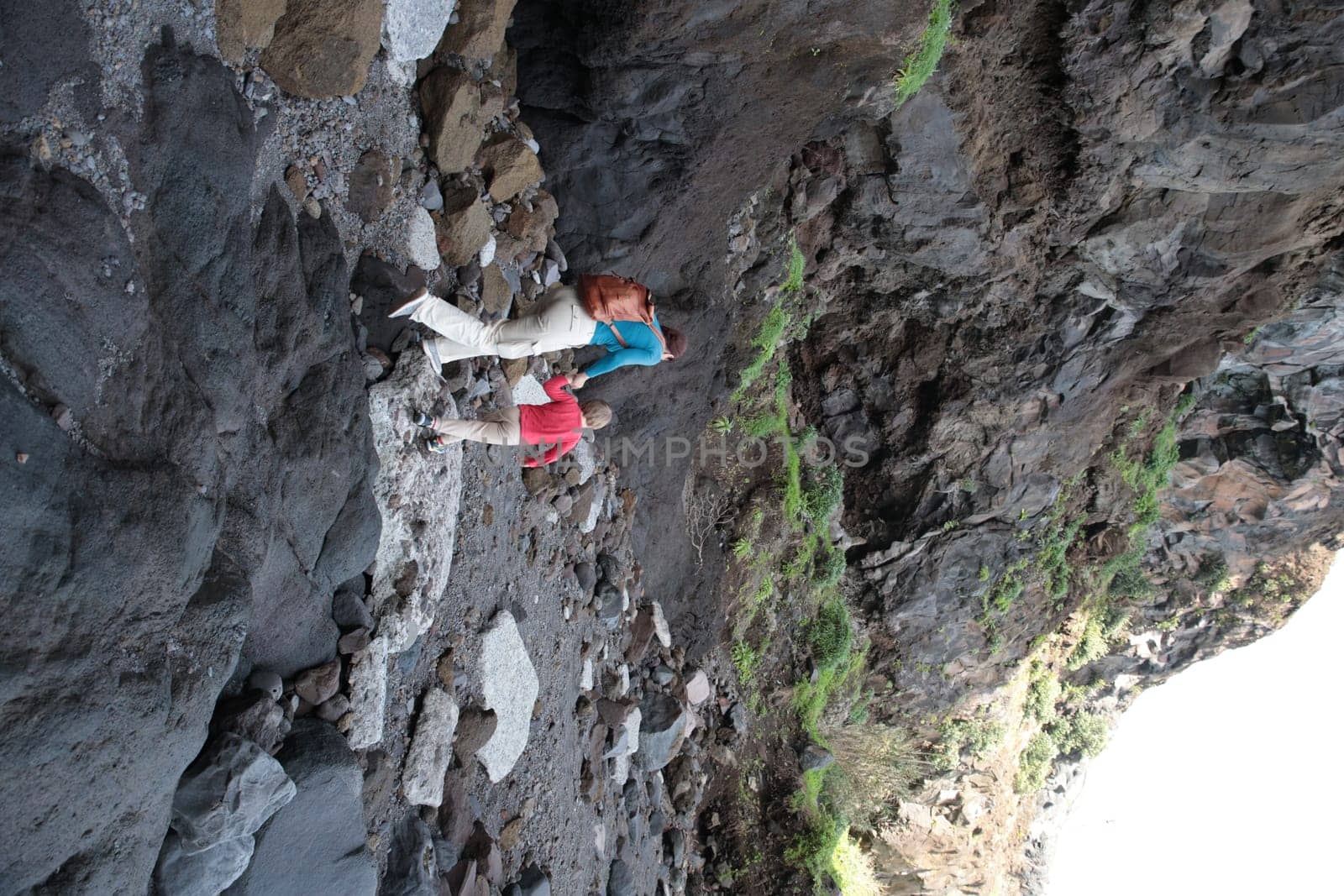 Two hikers exploring volcanic canyon walking on rocky path