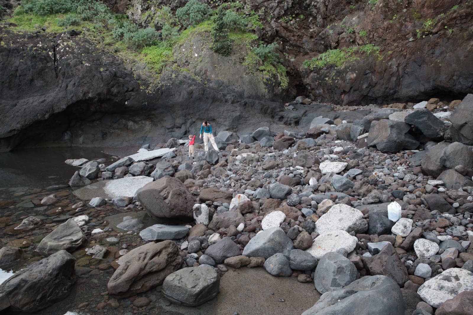 Tourists walking on rocky beach near the sea, exploring volcanic landscape