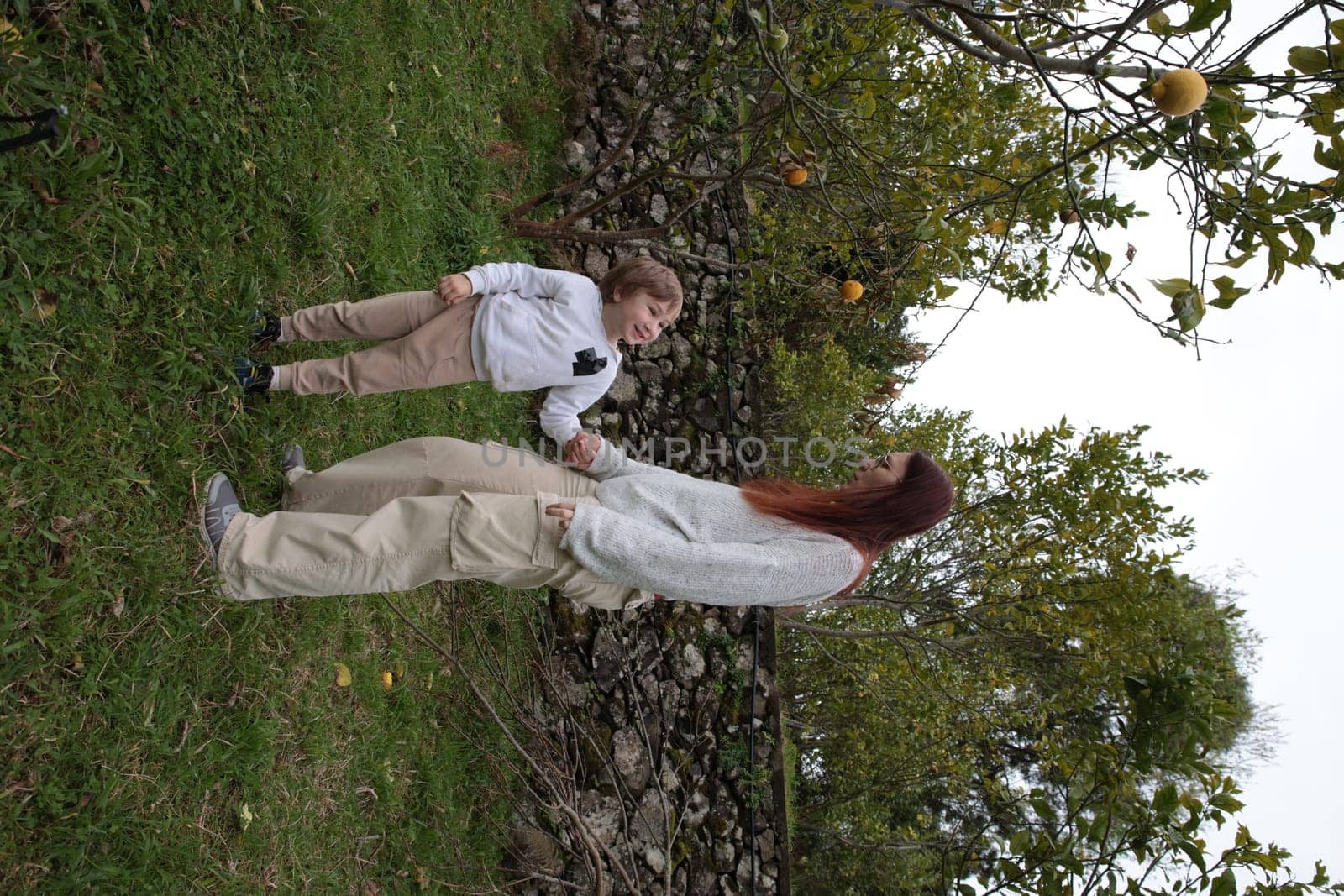 Mother and her son holding hands and looking at an orange tree in an orchard, enjoying a beautiful autumn day