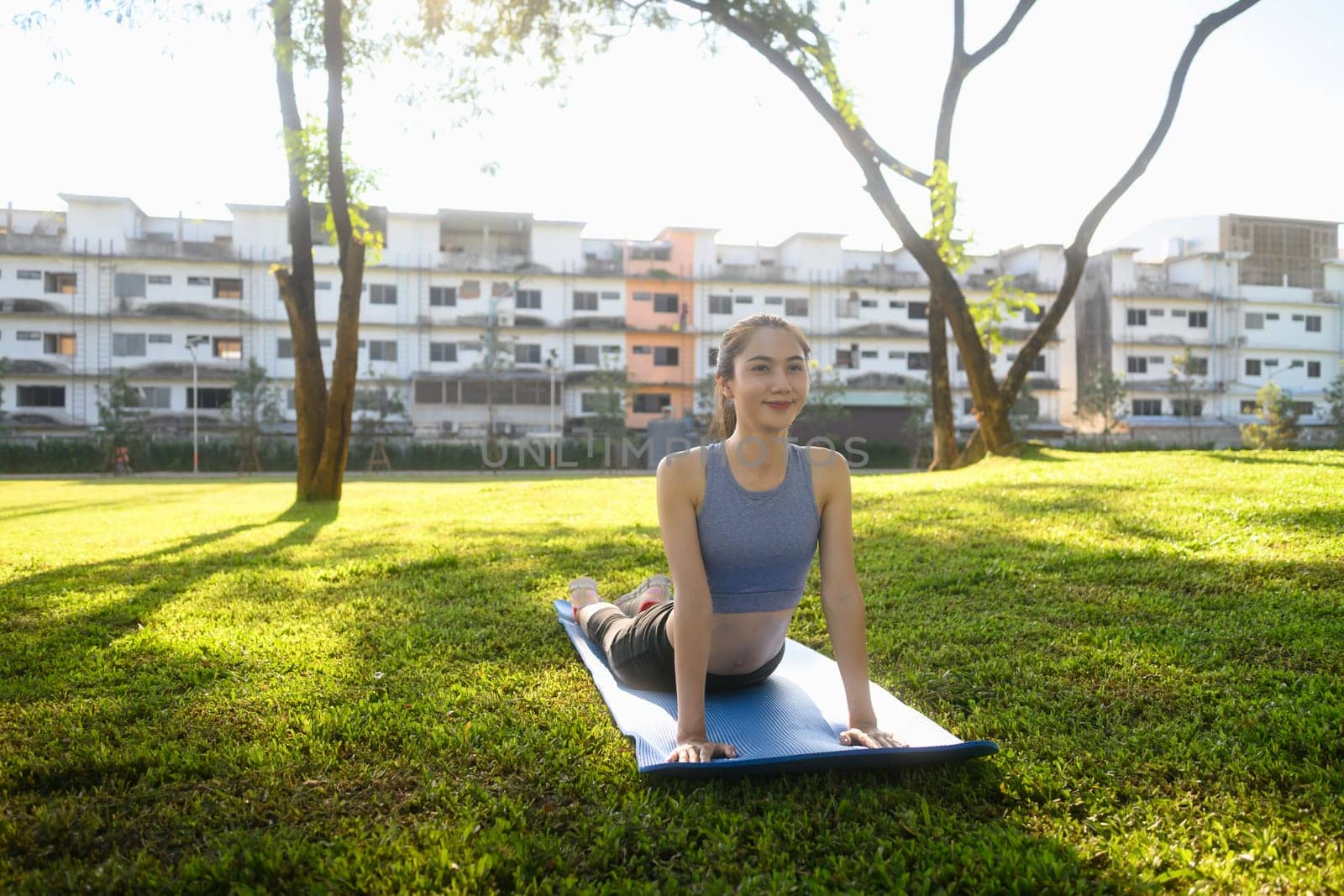 Beautiful woman practicing yoga in cobra pose on mat at a peaceful park.