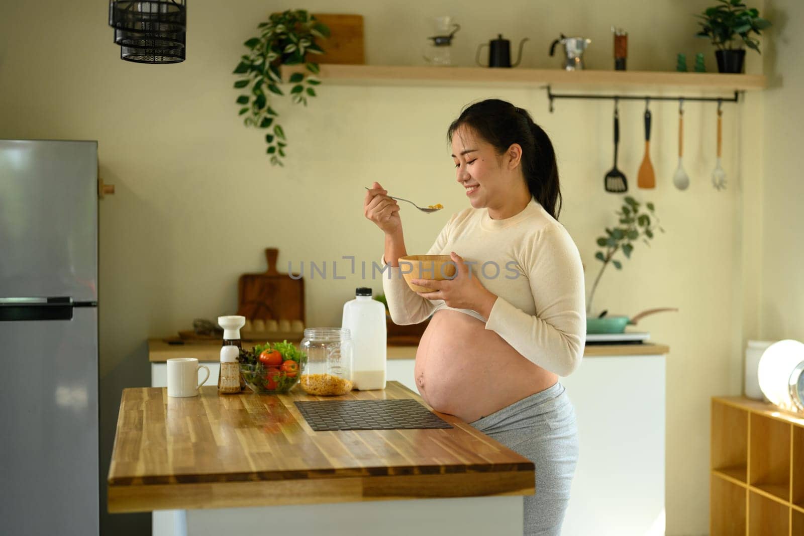 Smiling pregnant woman enjoying a bowl of corn flakes. Healthy pregnancy lifestyle concept.