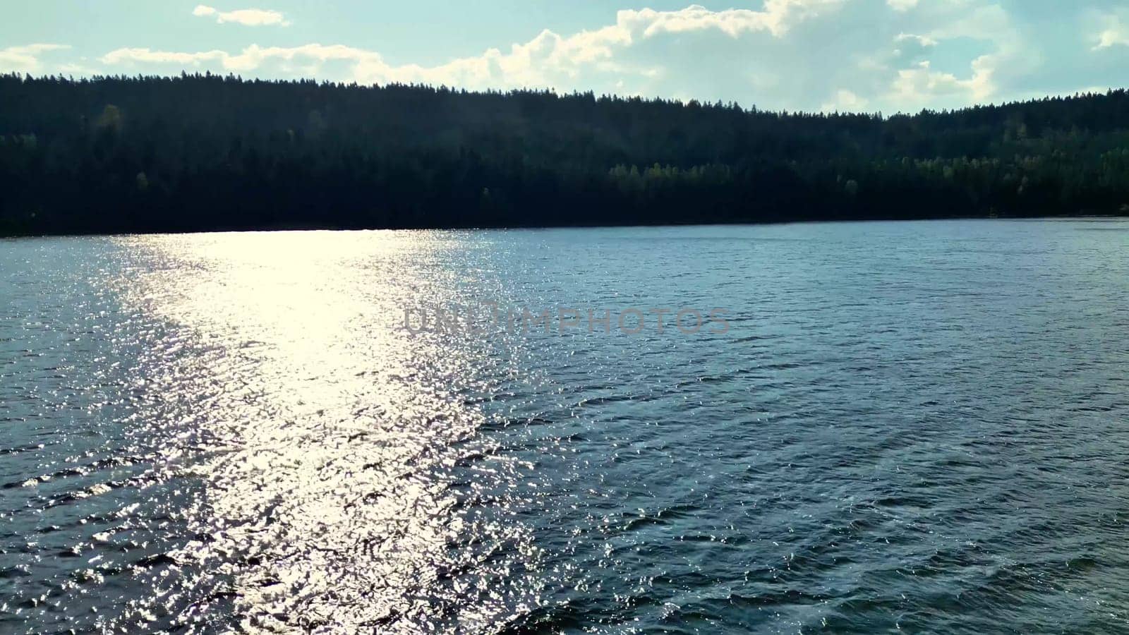 In this peaceful scene, a serene lake reflects the beautiful clear blue sky and distant rolling hills perfectly