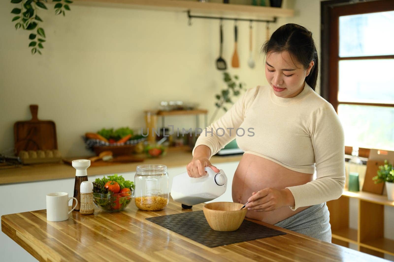 Pregnant woman preparing a healthy breakfast with cereal and milk in a bright kitchen.