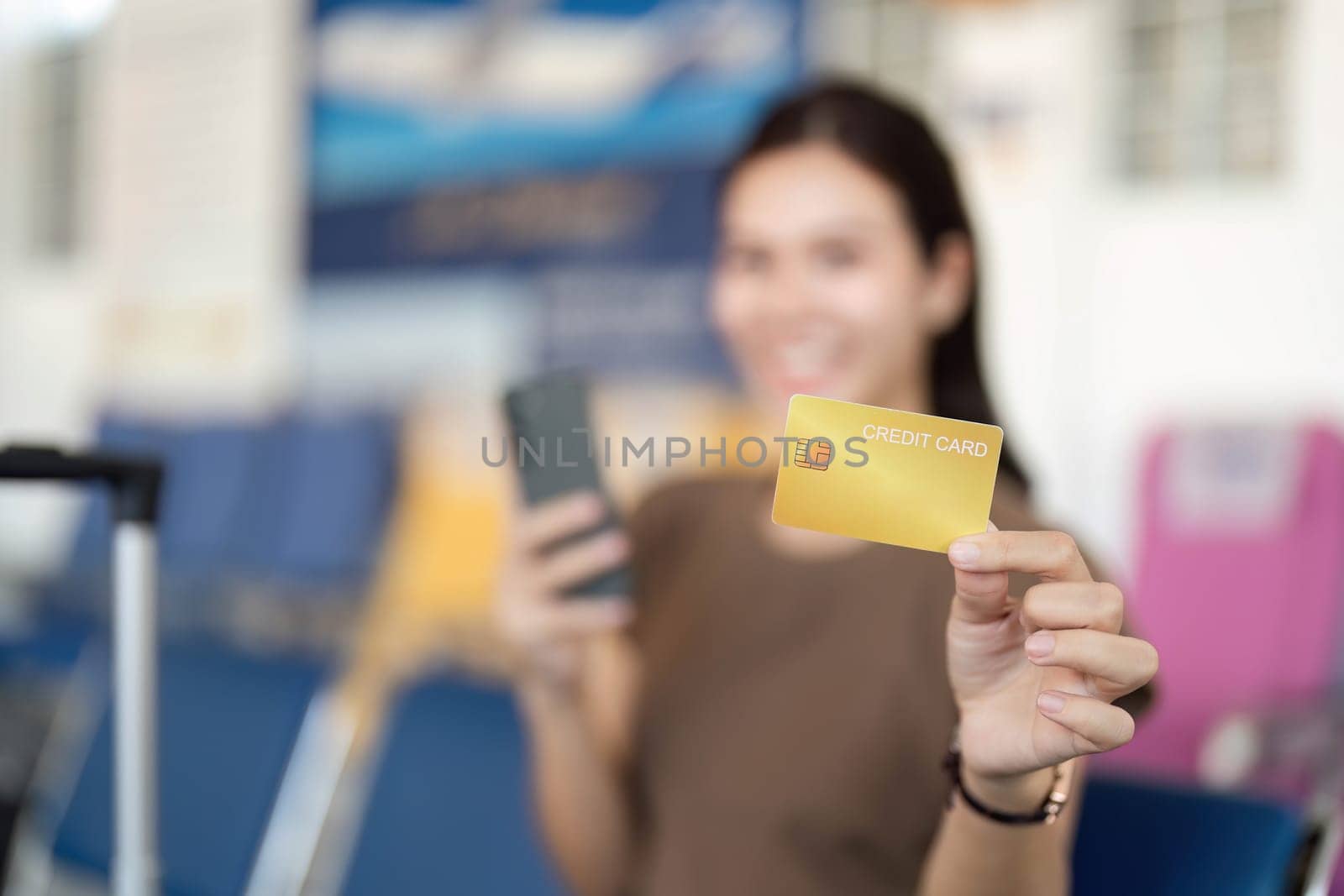 A young woman at the airport smiling brightly while holding a credit card, embodying the excitement of her travel journey.