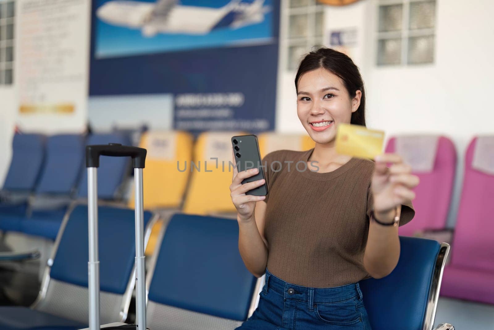 A joyful young woman at the airport, proudly holding a yellow card and phone, reflecting the joy of upcoming travels.