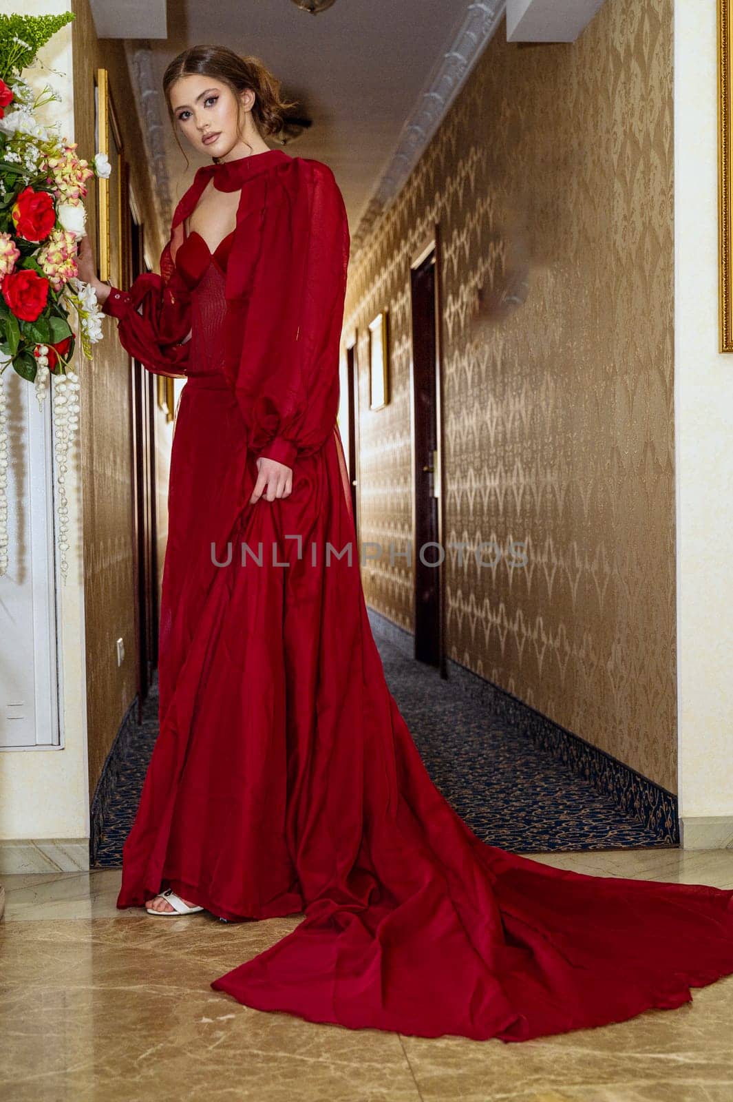 Model in red dress, elegant young woman in long evening dress. Beautiful girl with high hairstyle, shooting in hotel.