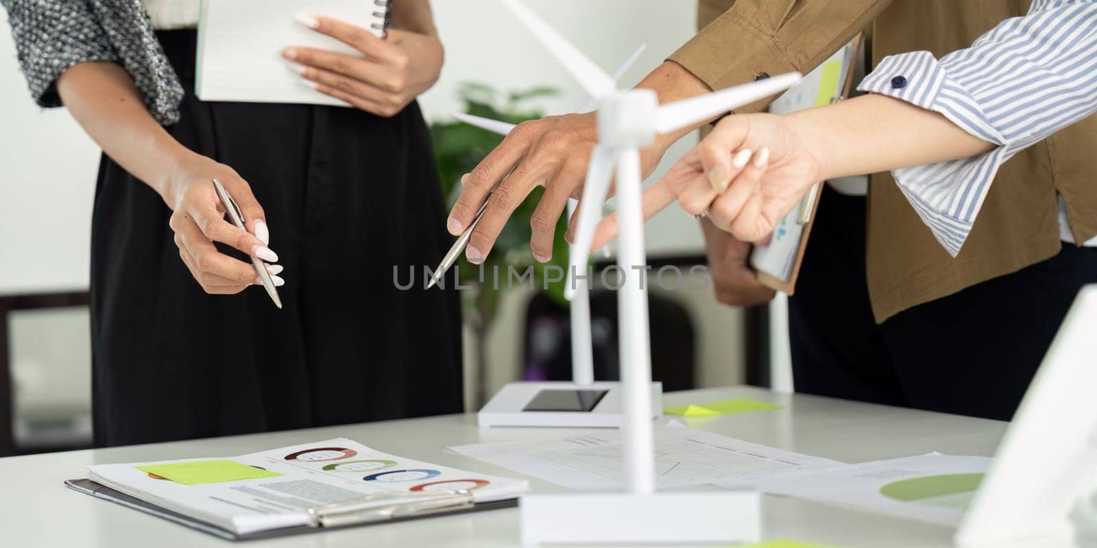 Team members actively collaborating and discussing plans for an ESG project, using visual data and wind turbine models as key elements in their strategy.