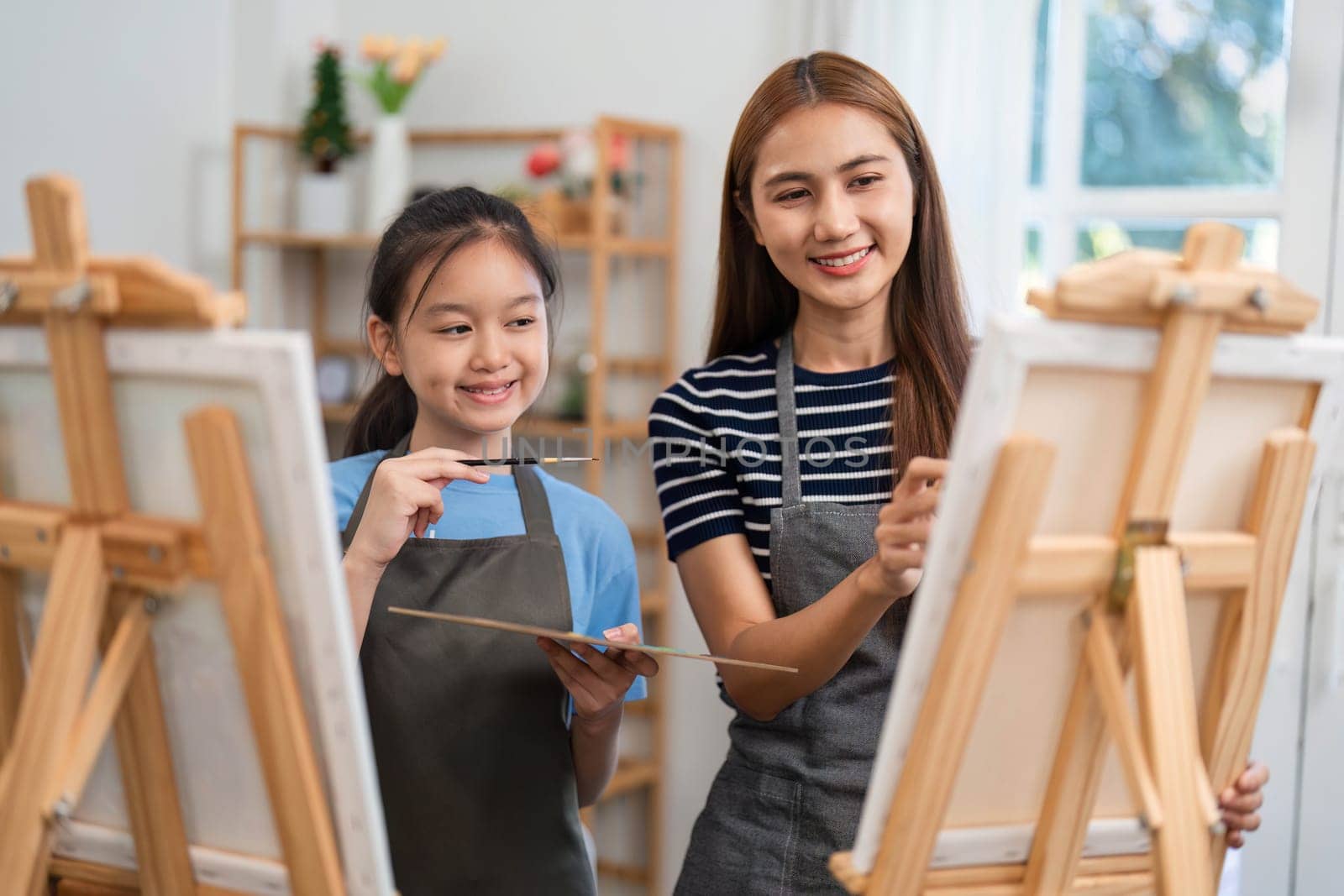A smiling mother and daughter painting together, sharing creativity and joy during a fun family time activity at home.
