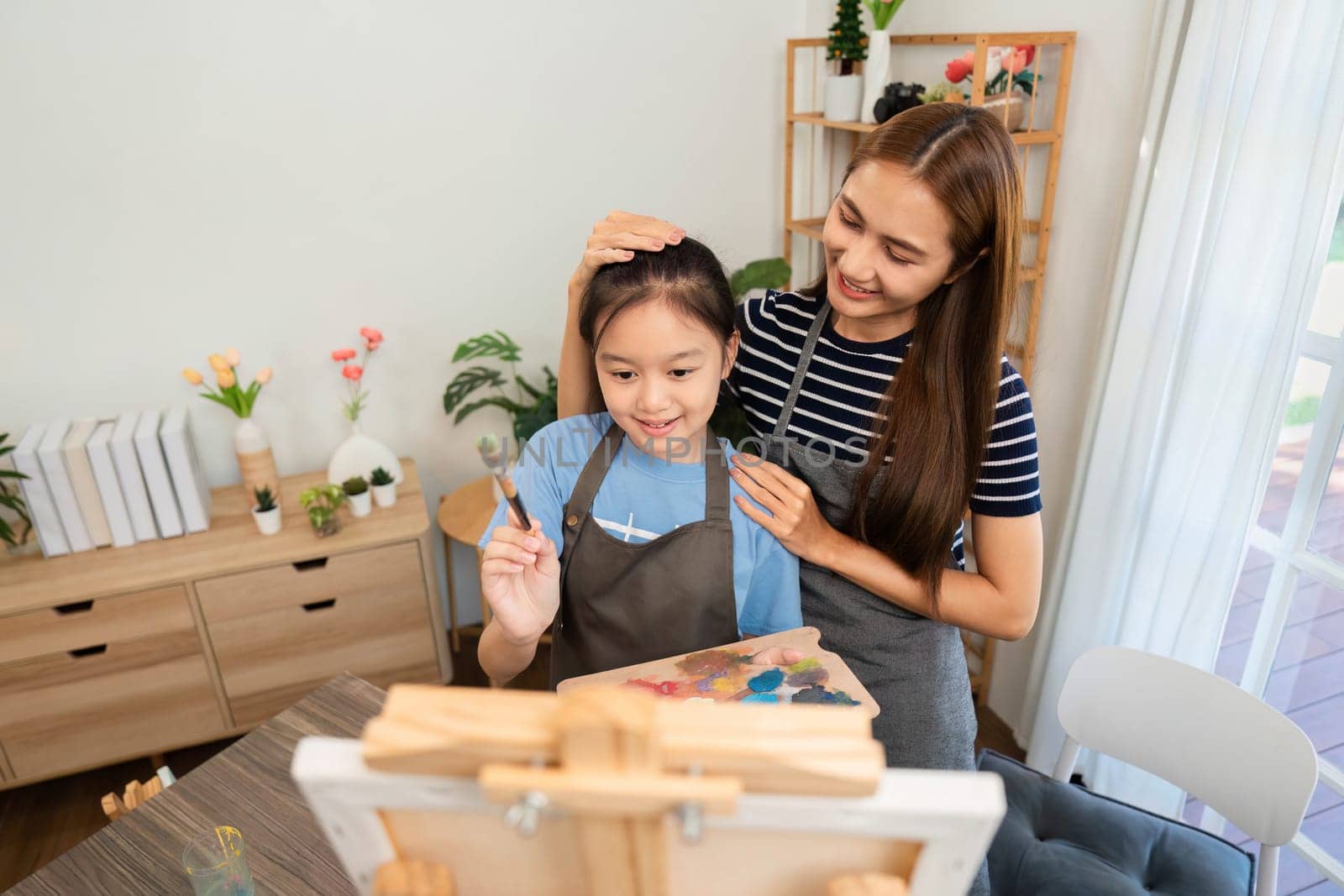 A heartwarming moment as a mother guides her daughter in painting, promoting artistic growth and enjoyment together.