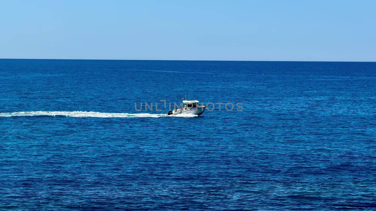 A sleek speedboat is elegantly slicing through the tranquil, blue ocean waters on a beautiful, sunny day