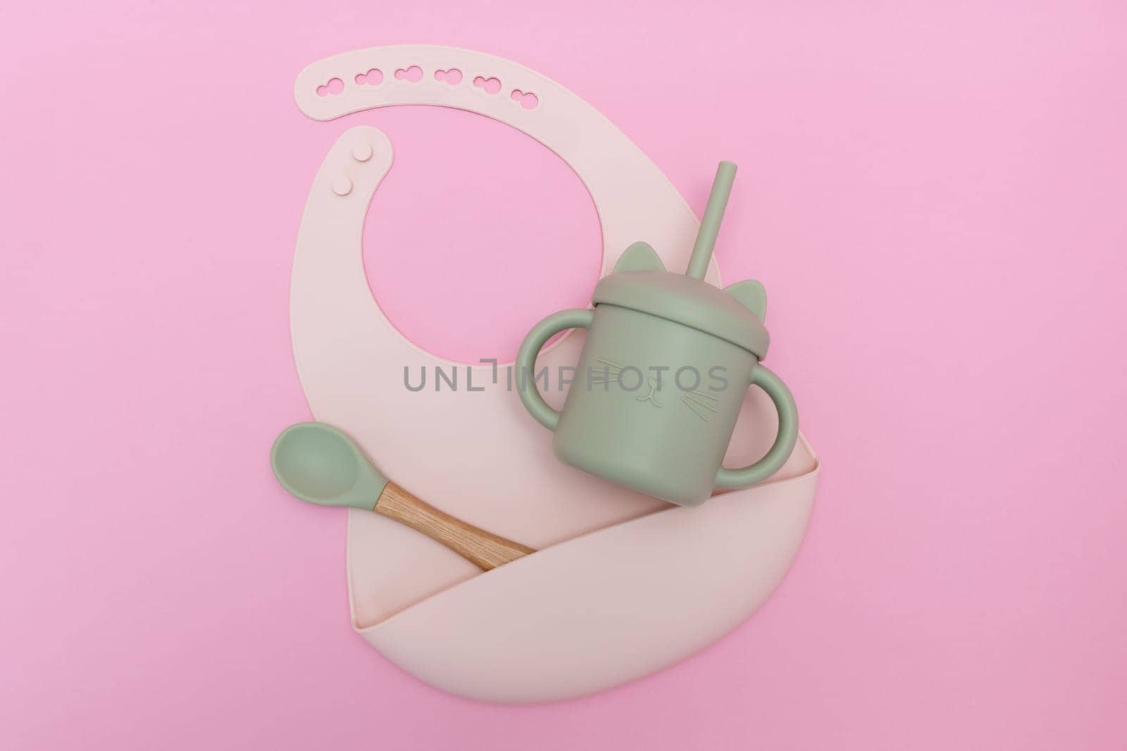 Modern pastel color set of silicone bib cups with straws and spoon on pink background. Baby tableware, first feeding, serving concept.