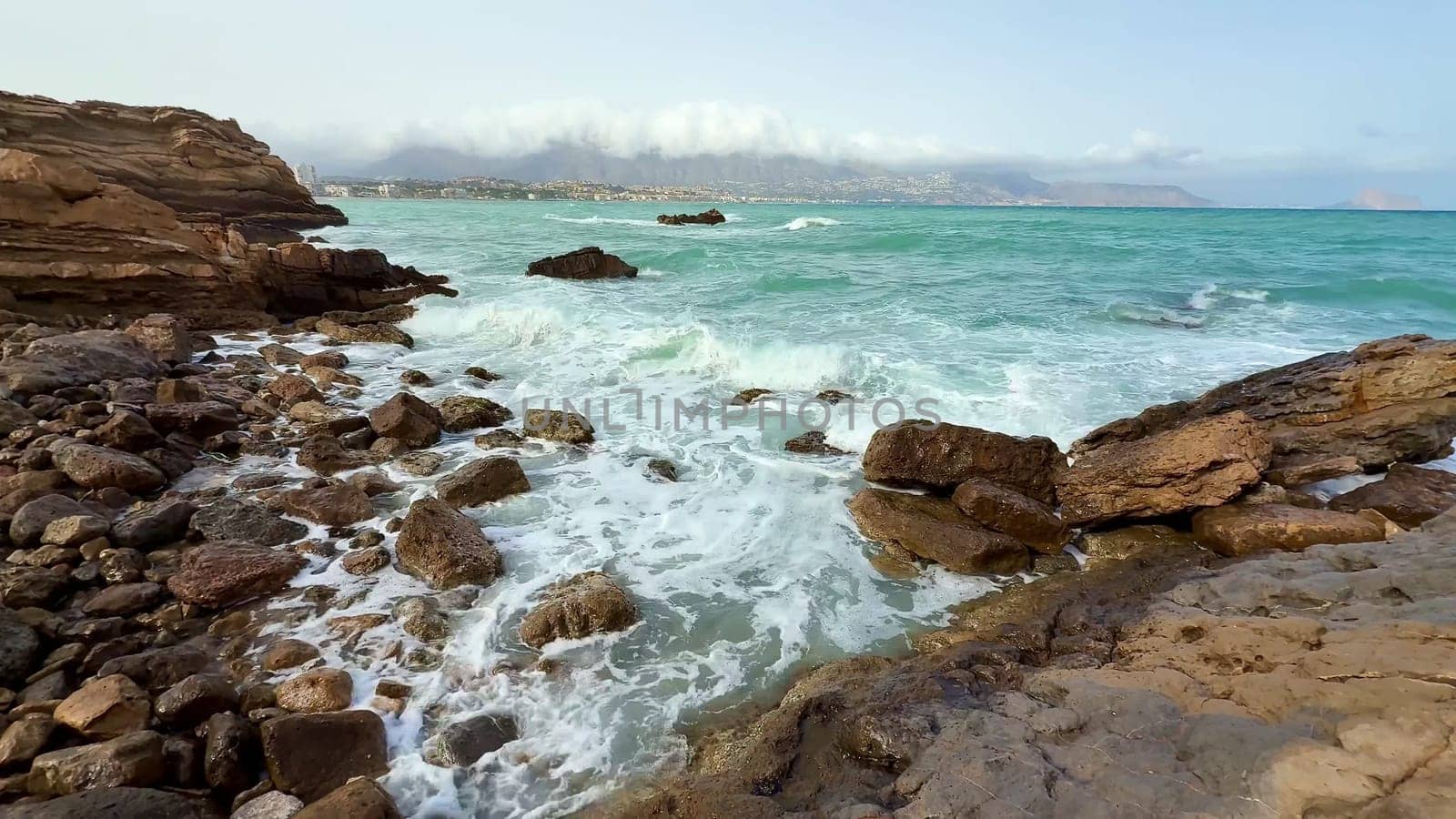 A tranquil coastal scene showcasing crashing waves against rocky cliffs while in the backdrop lies a clear blue sky