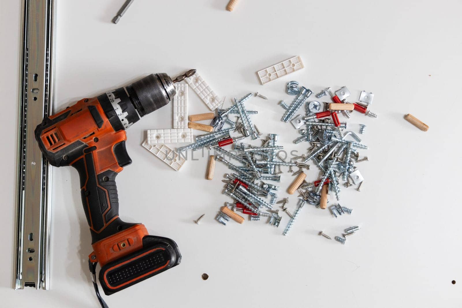 Electric screwdriver surrounded by various furniture fittings and hardware on clean white surface. Concept of home renovation, tools, and DIY assembly.