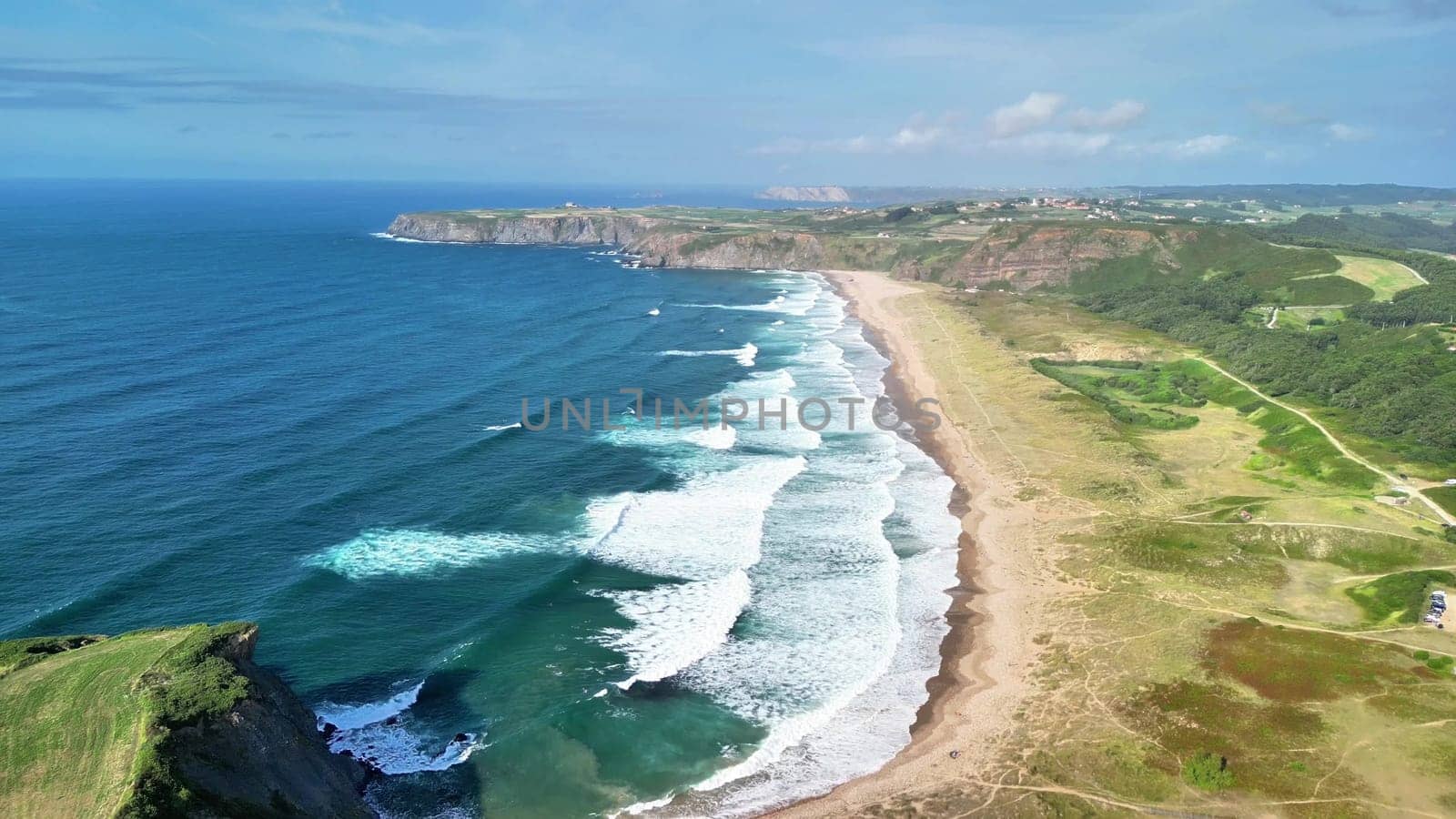 A stunning aerial shot beautifully capturing waves crashing energetically on the shore with lush green hills nearby
